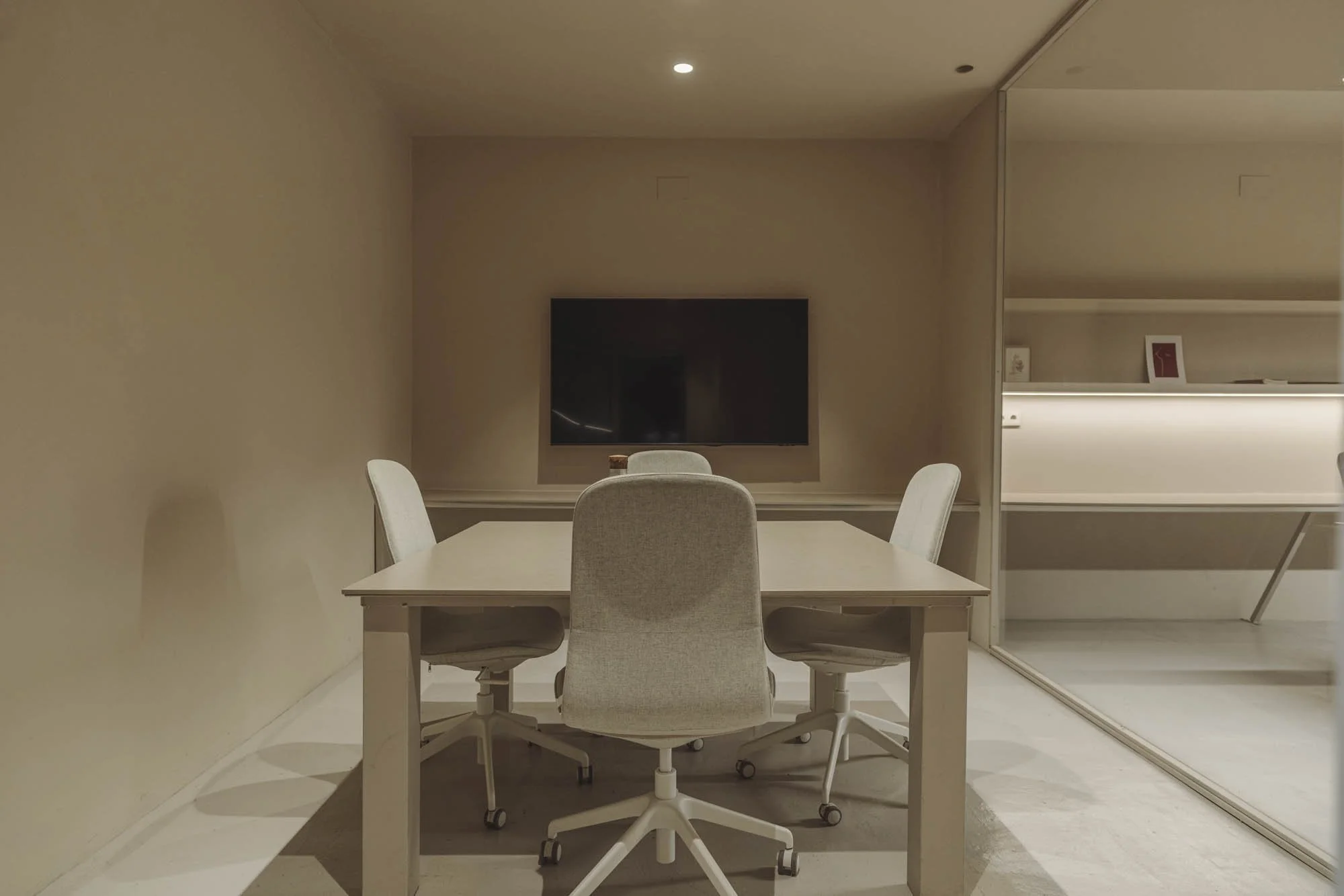 Sala de reuniones con una mesa, cuatro sillas y una pantalla plana en la pared de fondo.
