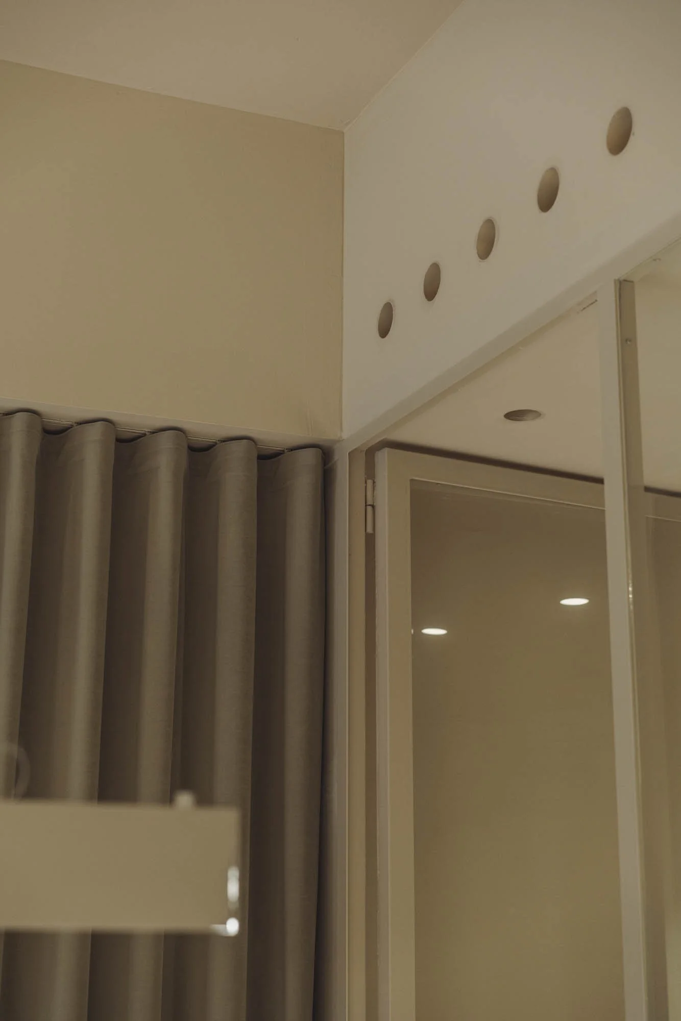 Vista interior mostrando una pared con varias perforaciones circulares y cortinas beige al lado de una puerta de vidrio.