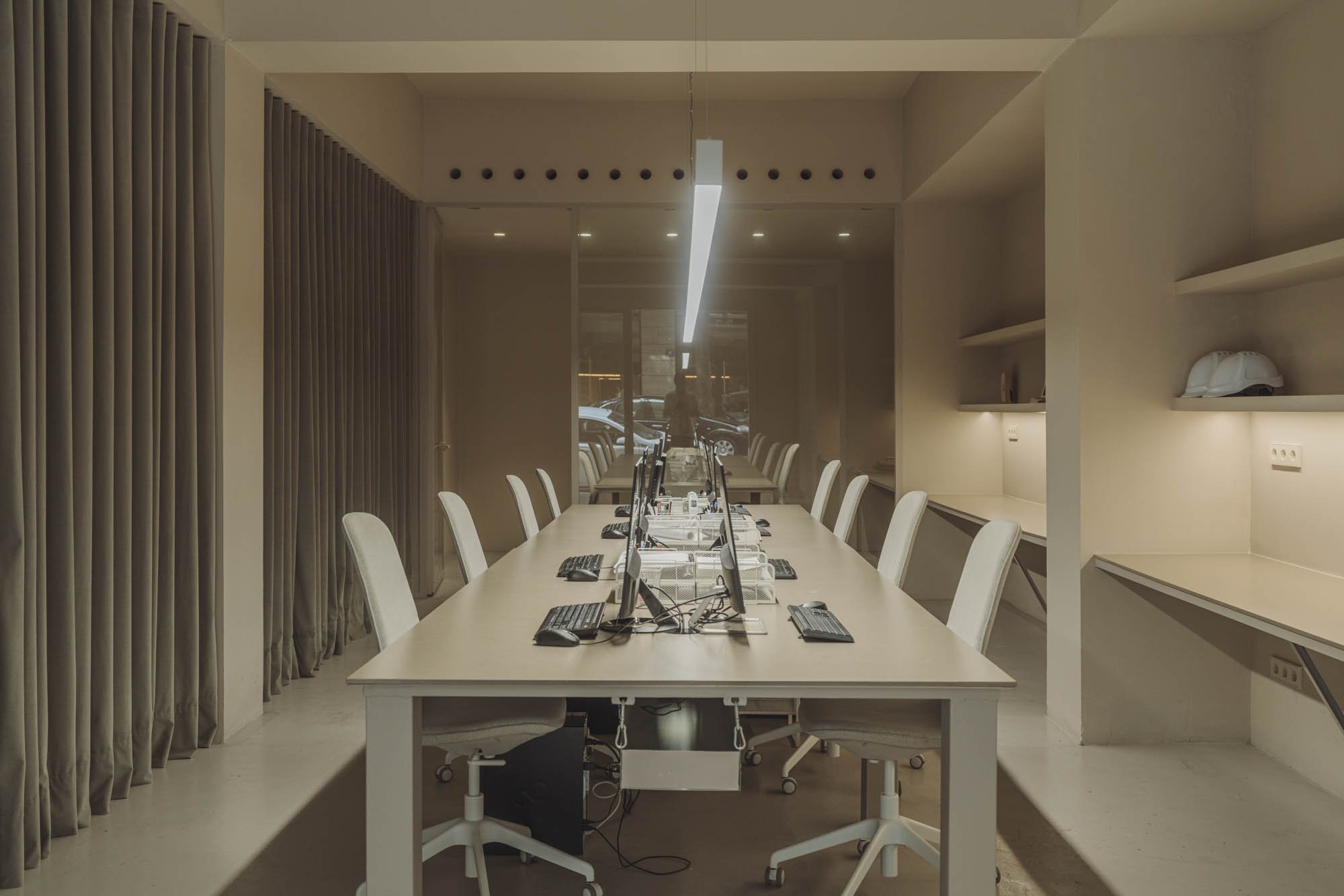 Sala de conferencias con varias computadoras en una mesa larga y sillas blancas.