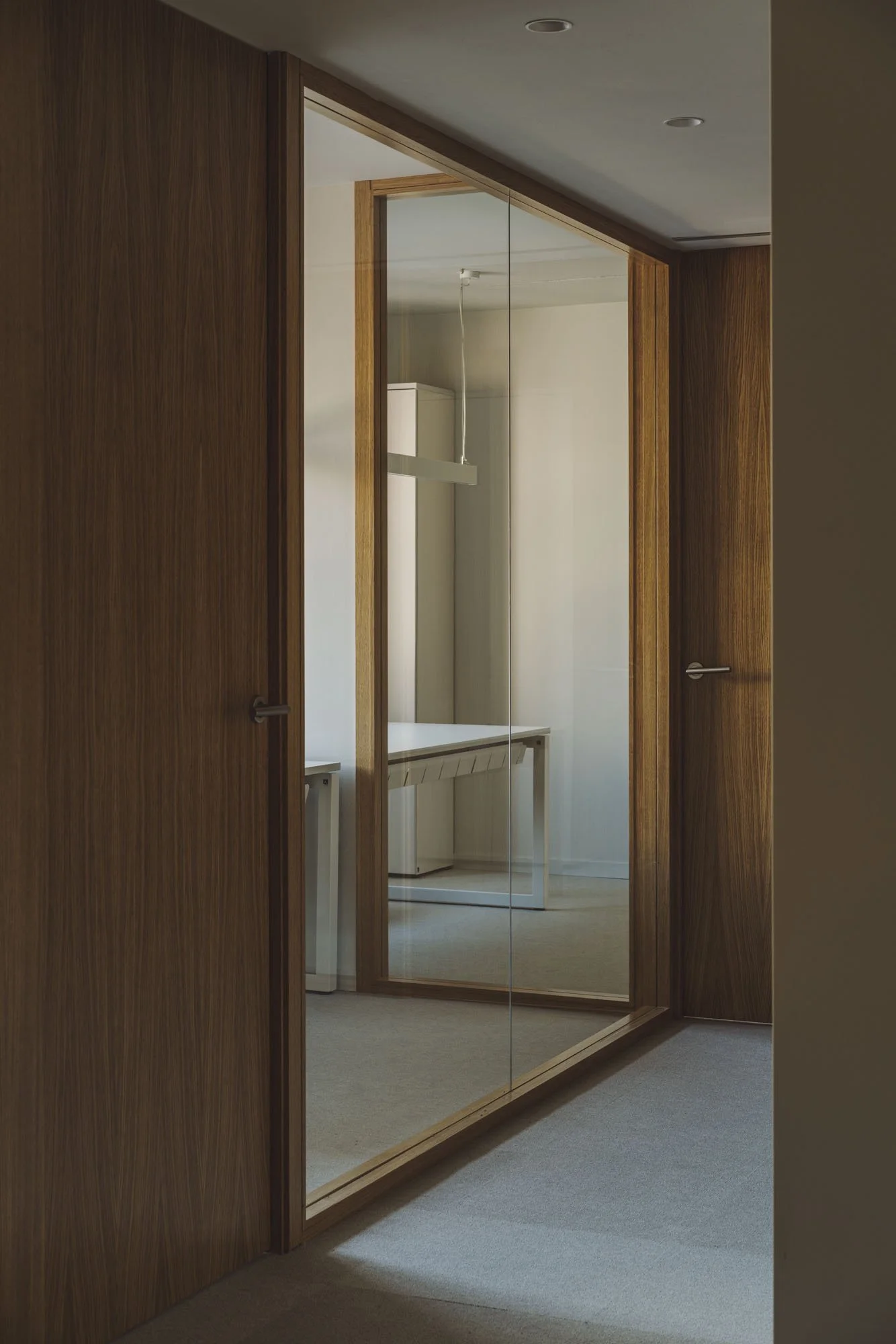 Puerta corredera de madera con espejo en el centro, reflejando un escritorio y una pared blanca.