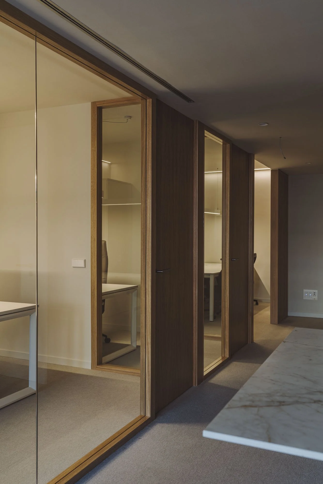 Oficinas con paredes de madera y puertas de vidrio, en un ambiente moderno y minimalista.