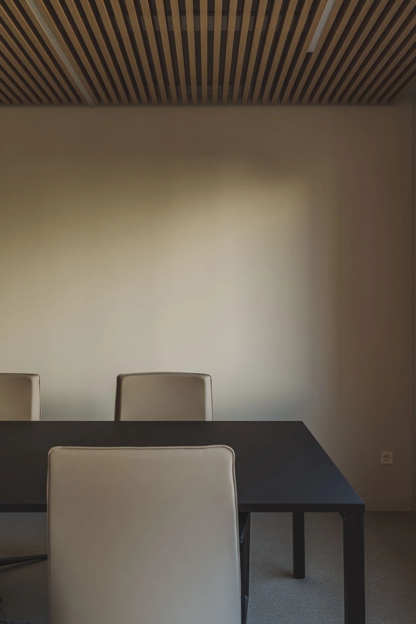 Sala de reuniones con mesa negra y sillas blancas, pared beige y techo de madera con listones.