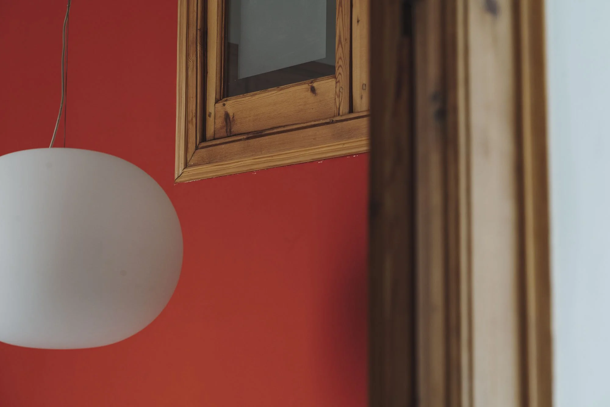 Lámpara blanca suspendida colgando frente a pared naranja y marco de madera en una habitación.