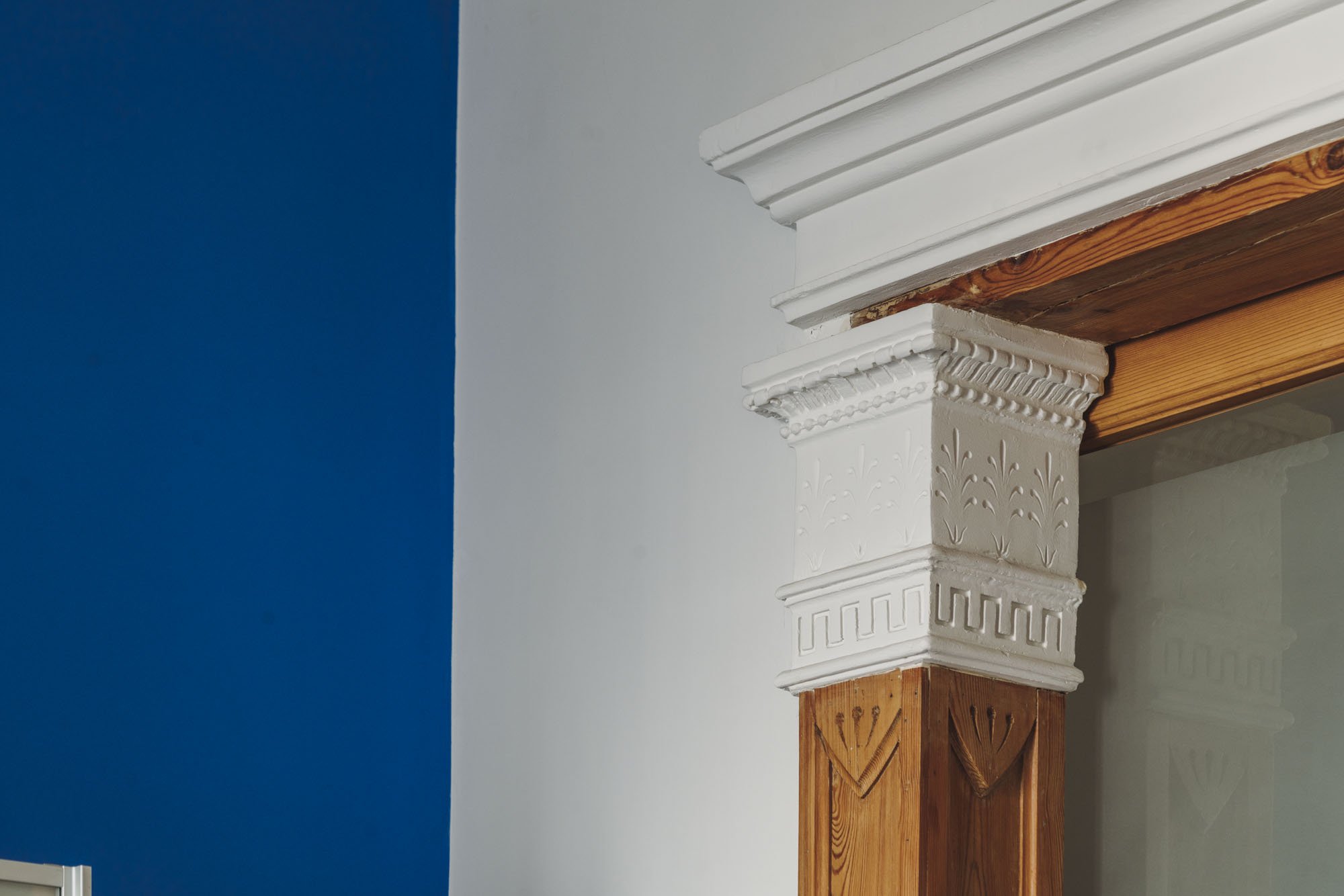 Detalle de un marco de chimenea con moldura decorativa en blanco y madera natural, con pared azul y blanca de fondo.