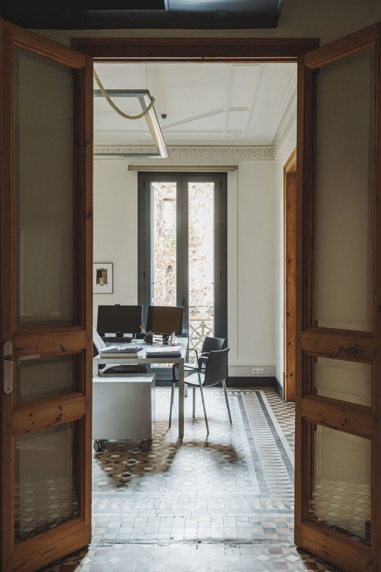 Oficina con escritorio, sillas, computadoras y ventana, vista desde una puerta de madera abierta
