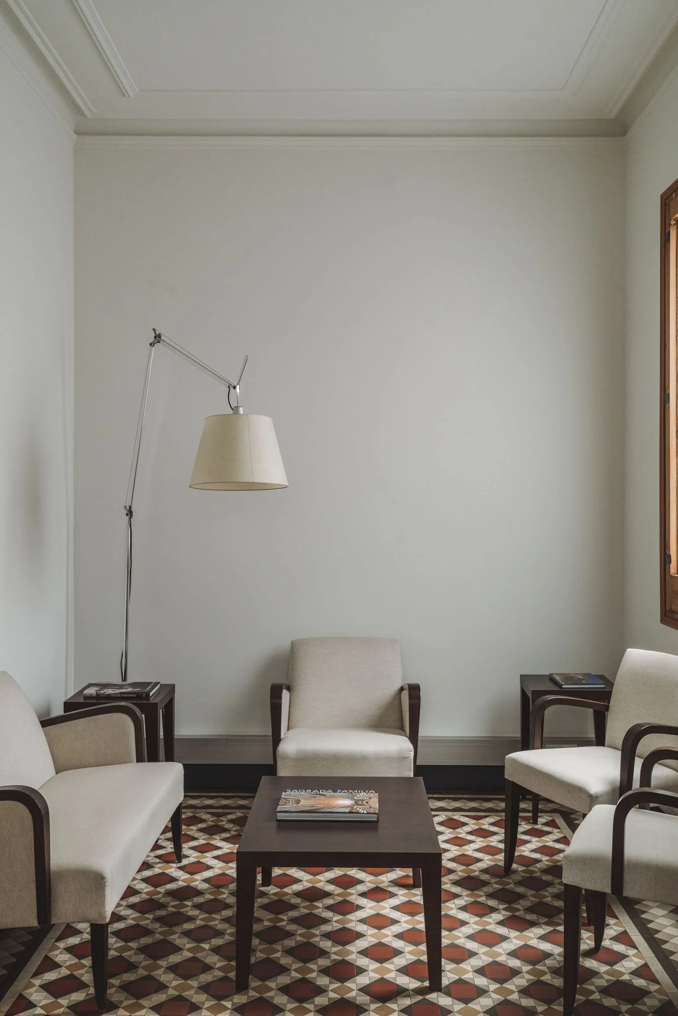 Sofá, sillas, mesas, lámpara de pie, libro en mesa, pared blanca, piso con azulejos decorativos.