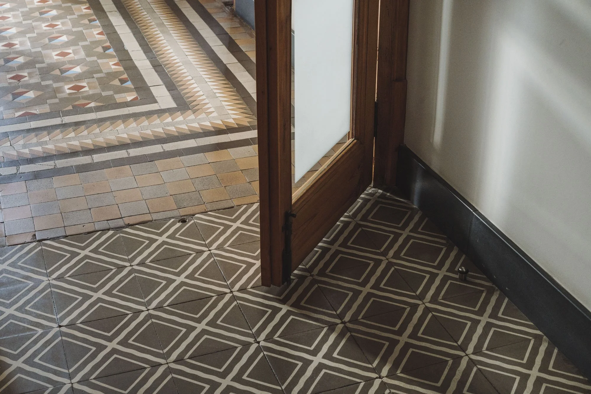 Suelo con mosaico geométrico marrón y beige y una entrada con piso de mosaico en tonos beige, gris y terracota, y madera en la puerta