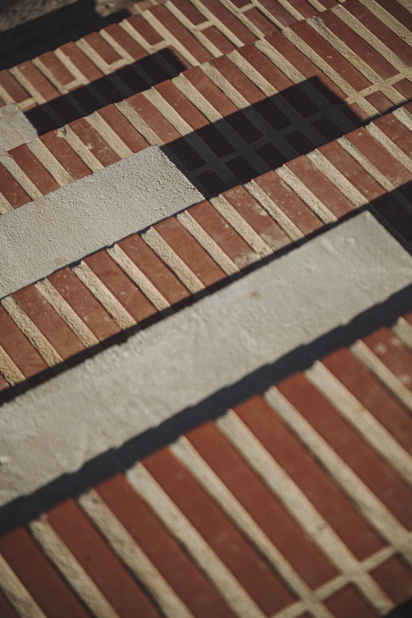 Patrón de ladrillos rojos y bloques de concreto en un muro con sombras al sol.