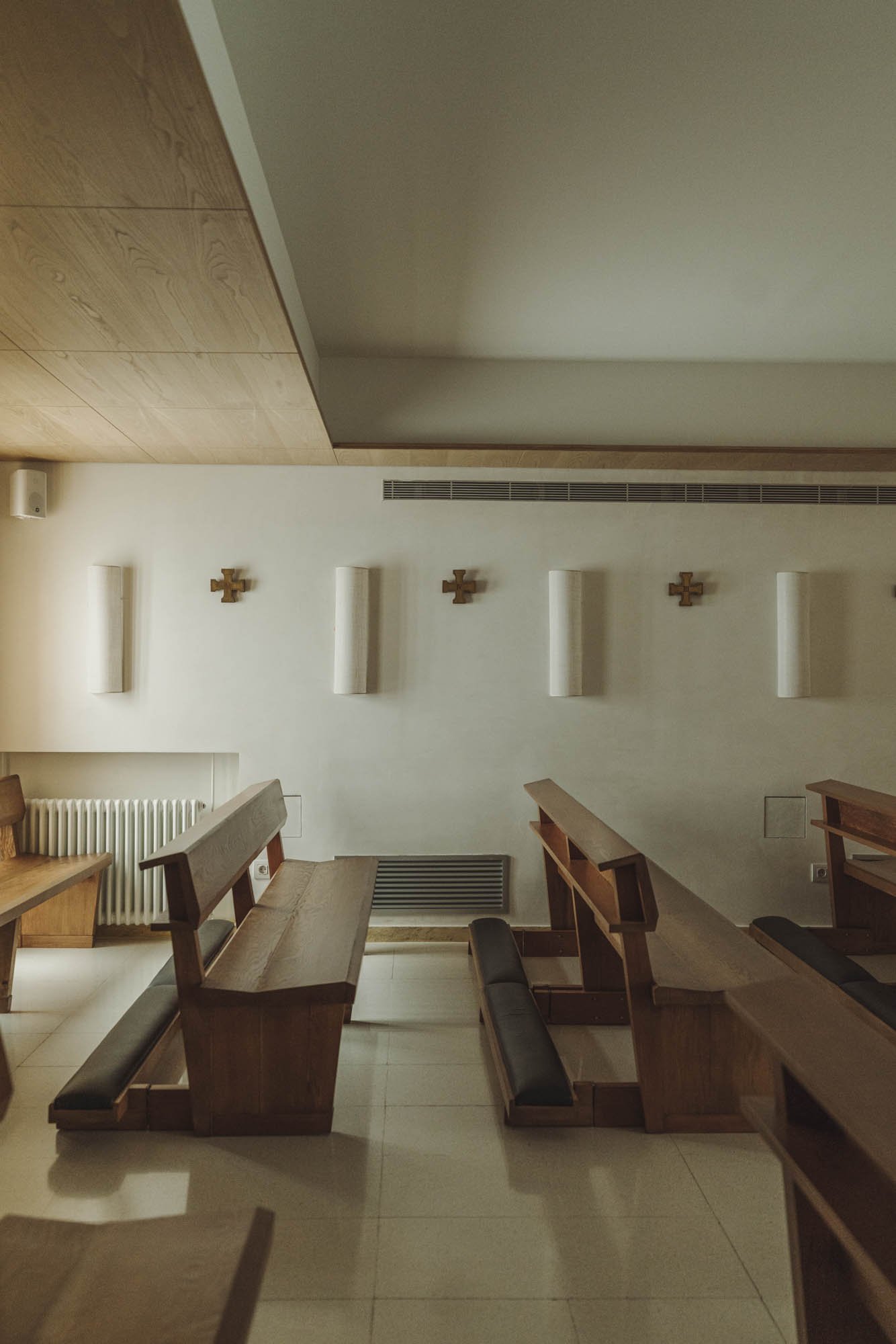 Interior de una capilla con bancos de madera, decoraciones en la pared y un radiador.