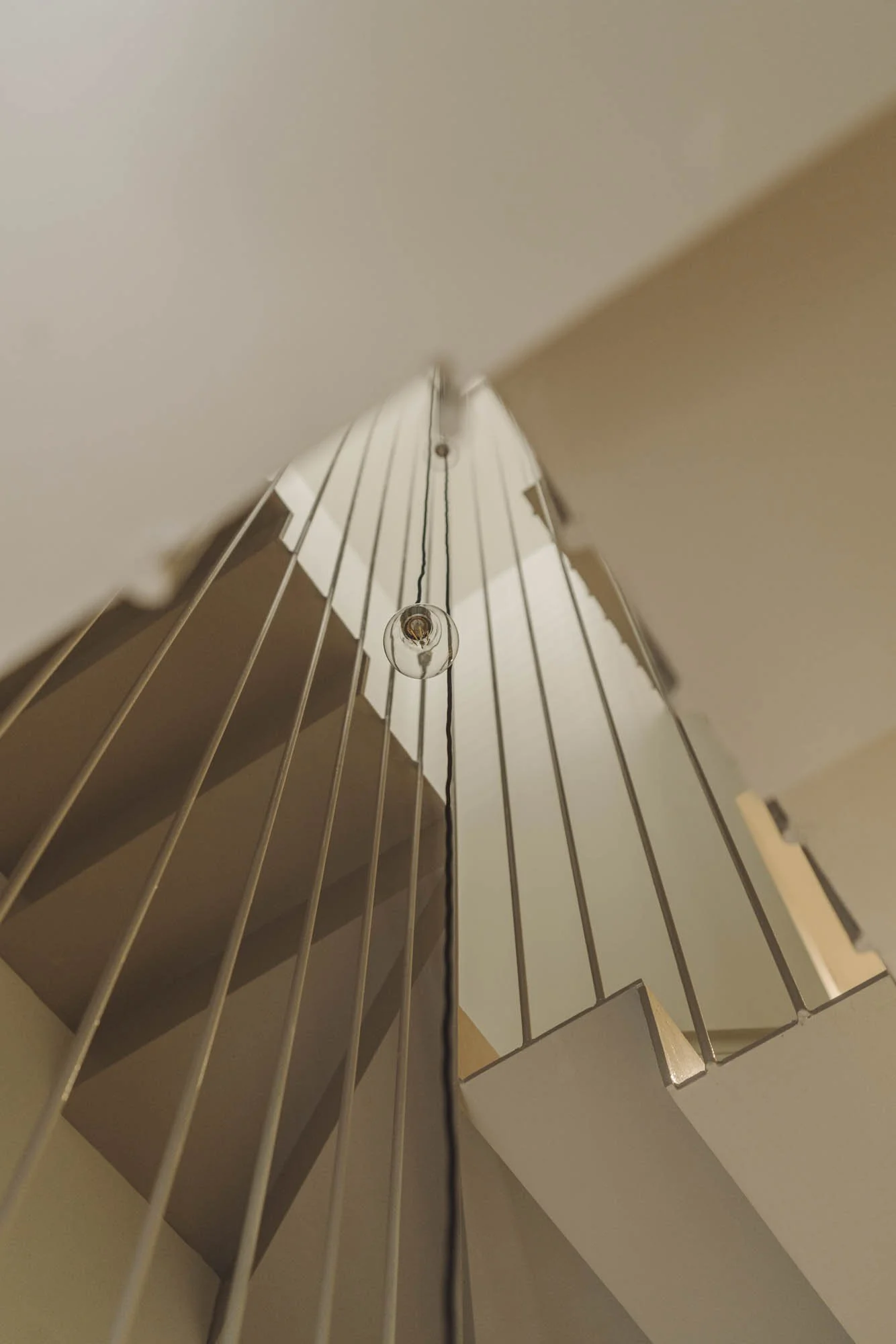 Perspectiva desde abajo de una lámpara colgante con bombilla expuesta y rejas blancas en un techo de interior.