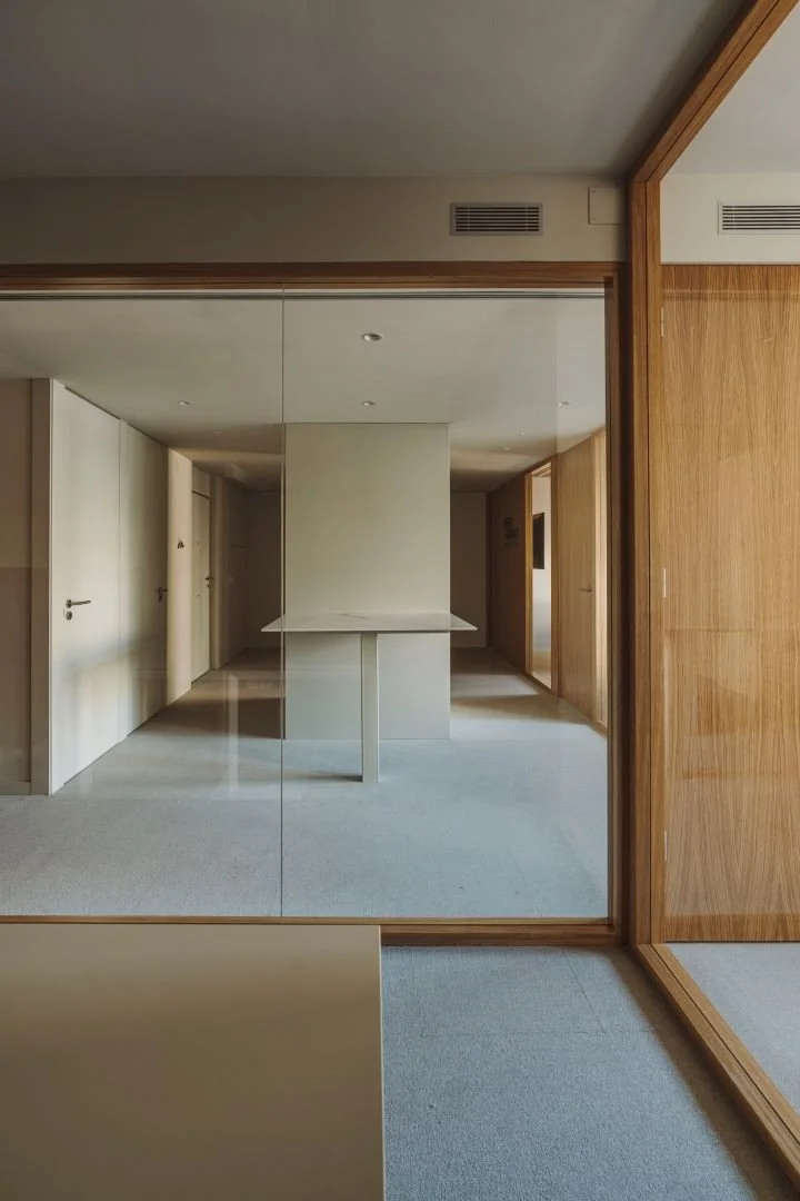 Vista de un espacio interior con paredes de madera, un espejo grande que refleja la habitación, puertas blancas y una pared central con estructura de madera.