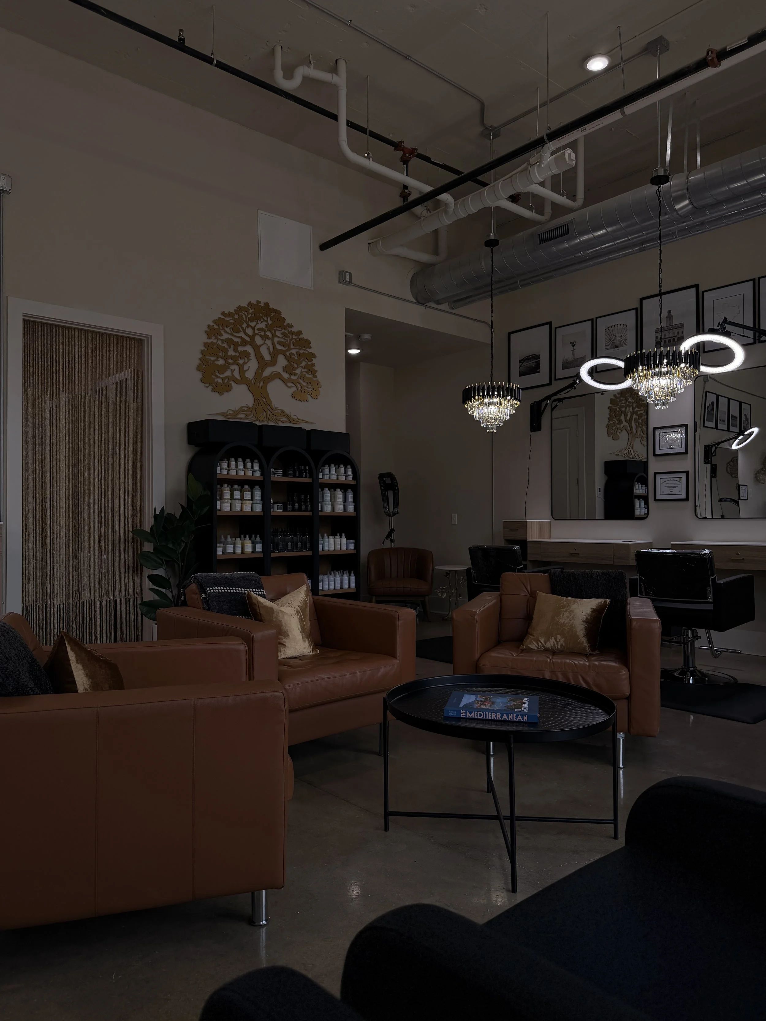Modern salon lounge area with brown leather sofas, a black coffee table with a book, wall art, and pendant lights.