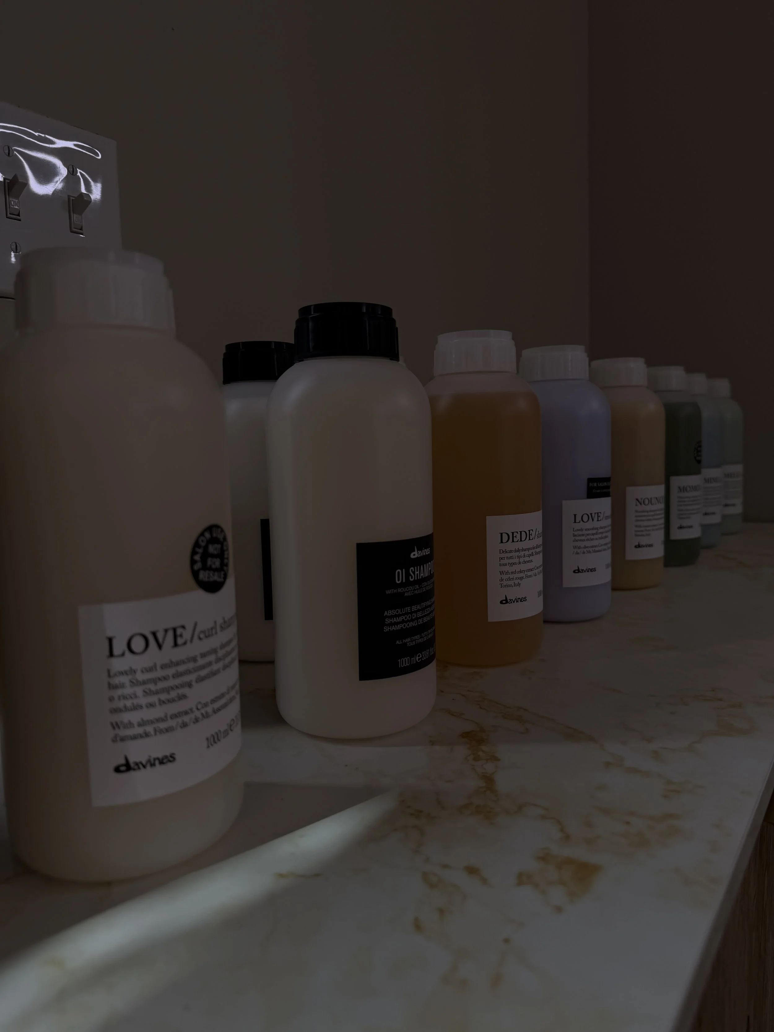 Line of various pastel-colored bottles on a marble countertop in a dimly lit room.