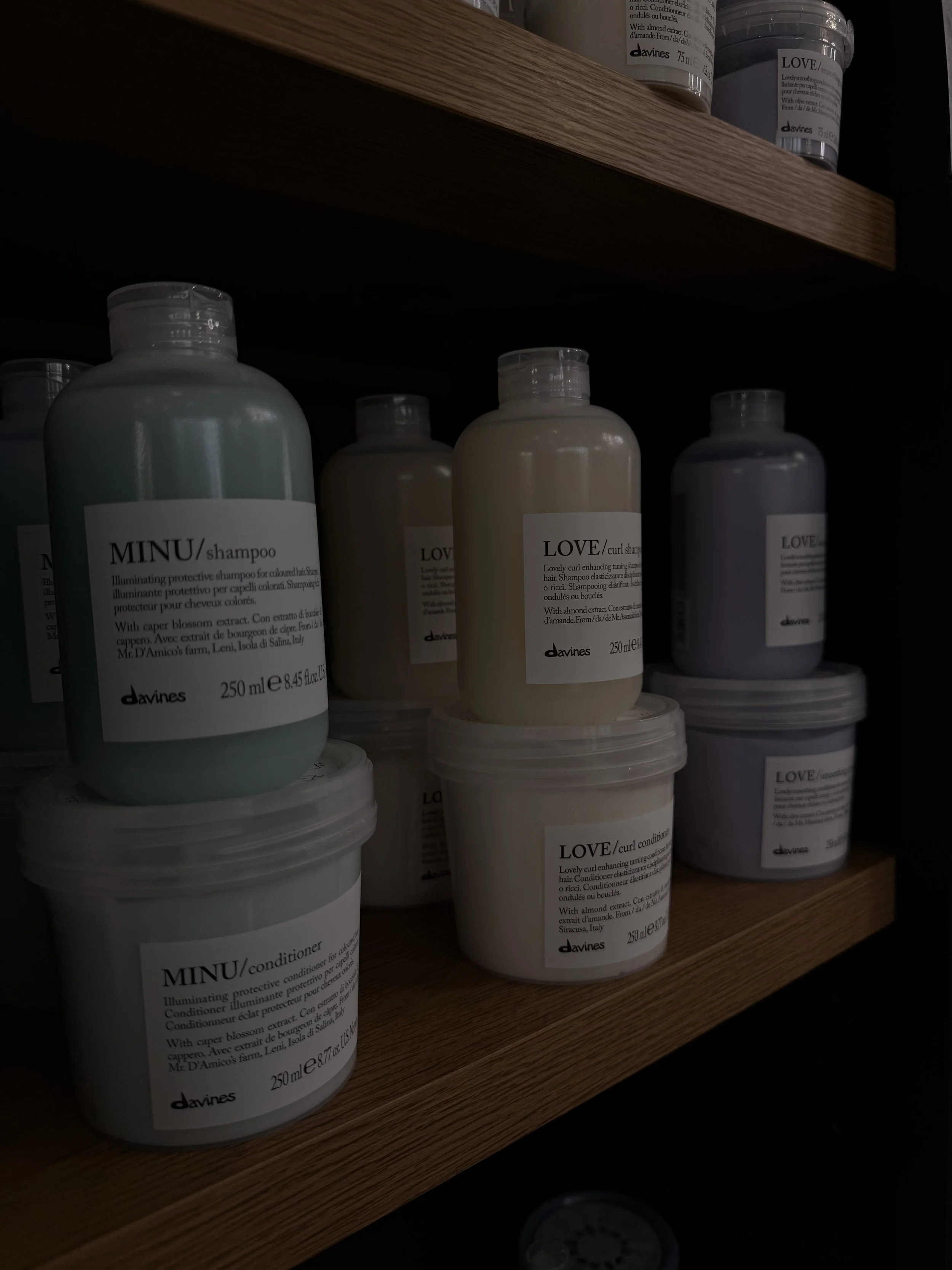Several bottles and containers of Davines hair care products, including shampoo, conditioner, and curl cream, on a wooden shelf.
