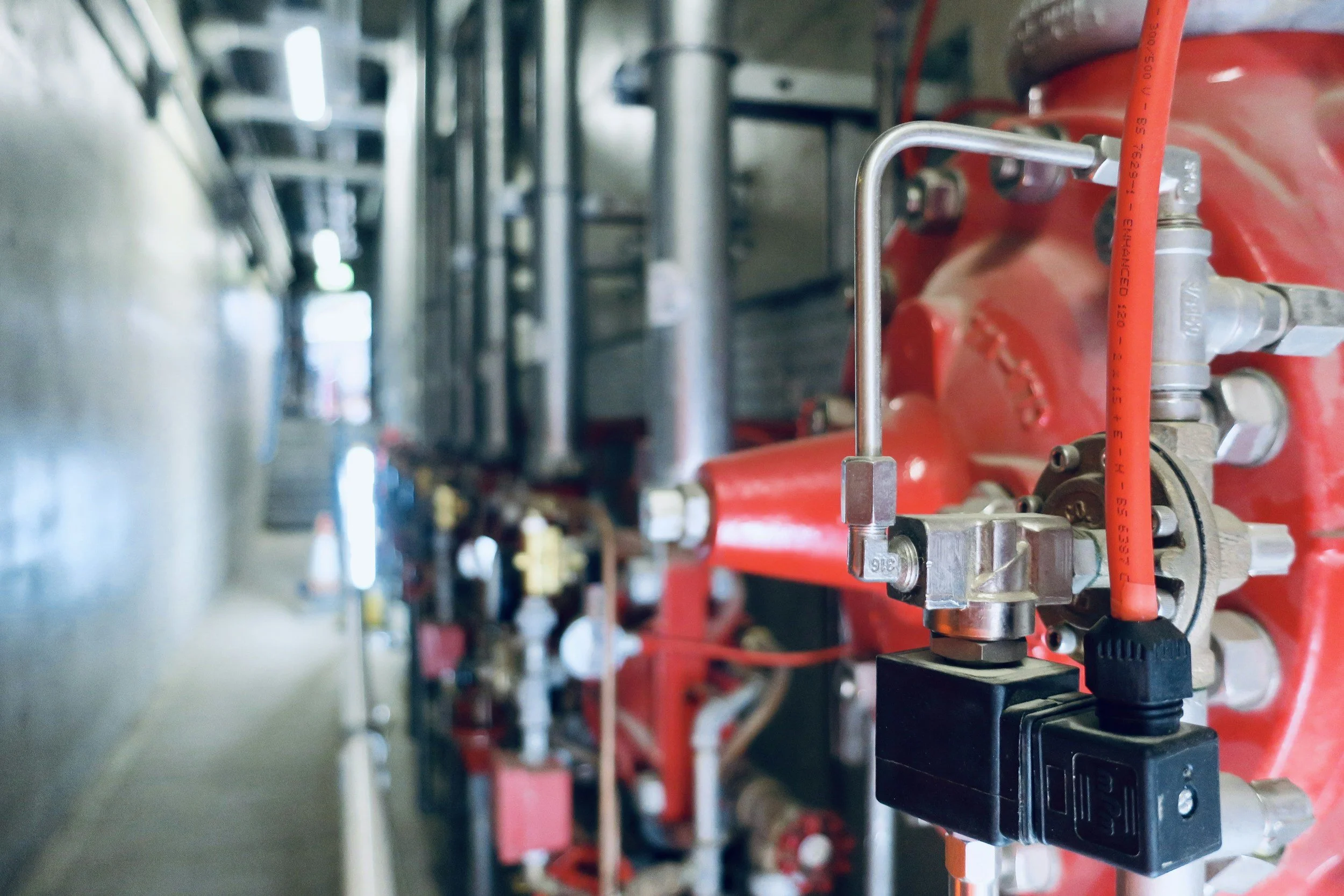 Close-up of fire sprinkler system piping with a red valve and metallic fittings on a wall in a fire safety room.