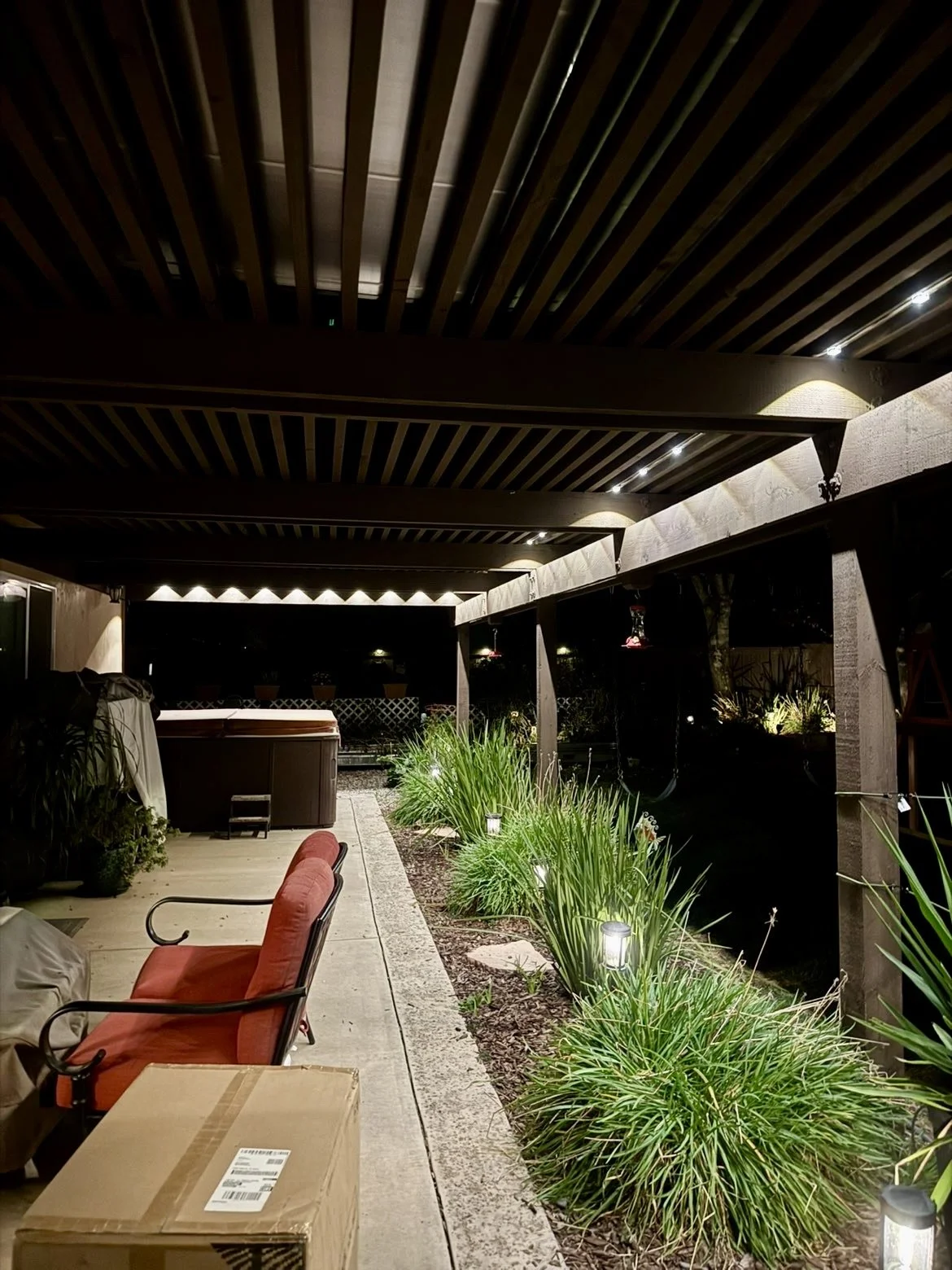 Nighttime patio with outdoor seating, plants, and pathway lighting.