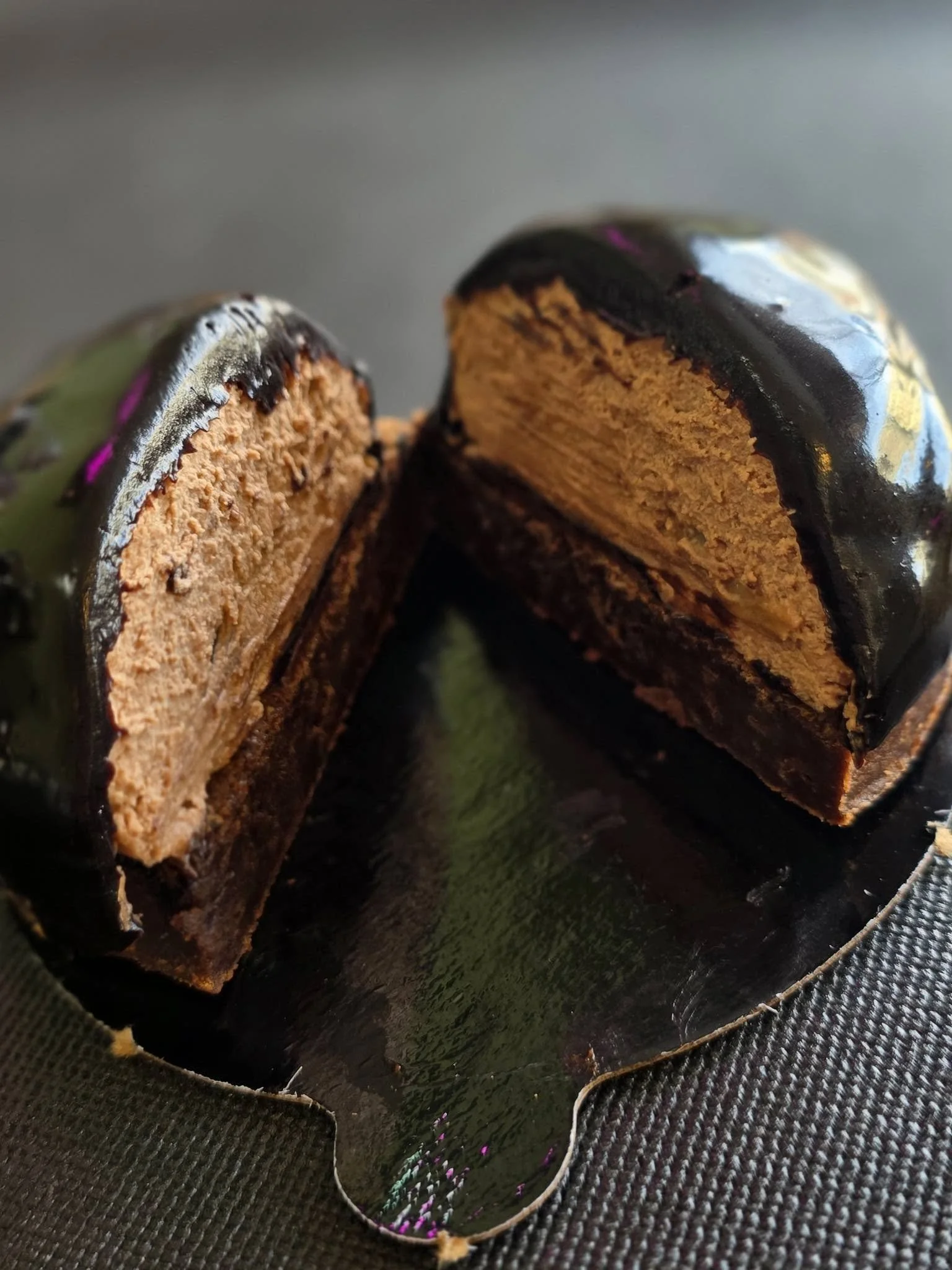 Cross-section of a layered chocolate and peanut butter cake with a shiny chocolate glaze on top, placed on a reflective black surface.