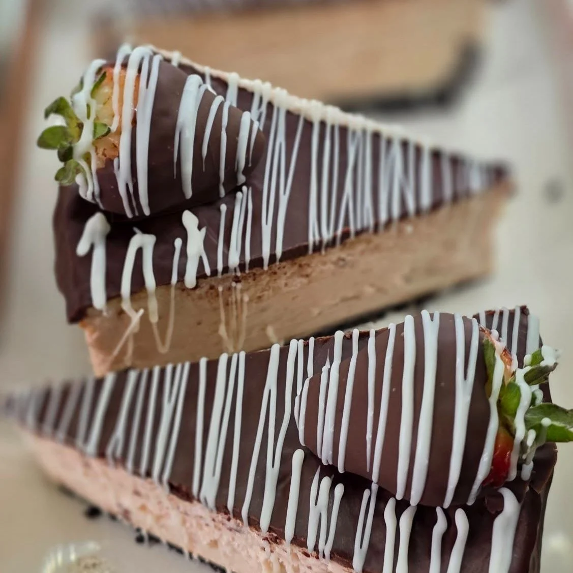 Close-up of two chocolate-covered strawberry and cream layered desserts decorated with white chocolate drizzle.