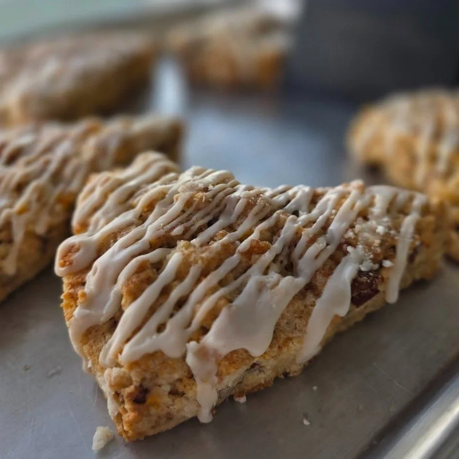 Close-up of a baked pastry drizzled with white icing on a metal tray, with other similar pastries in the background.