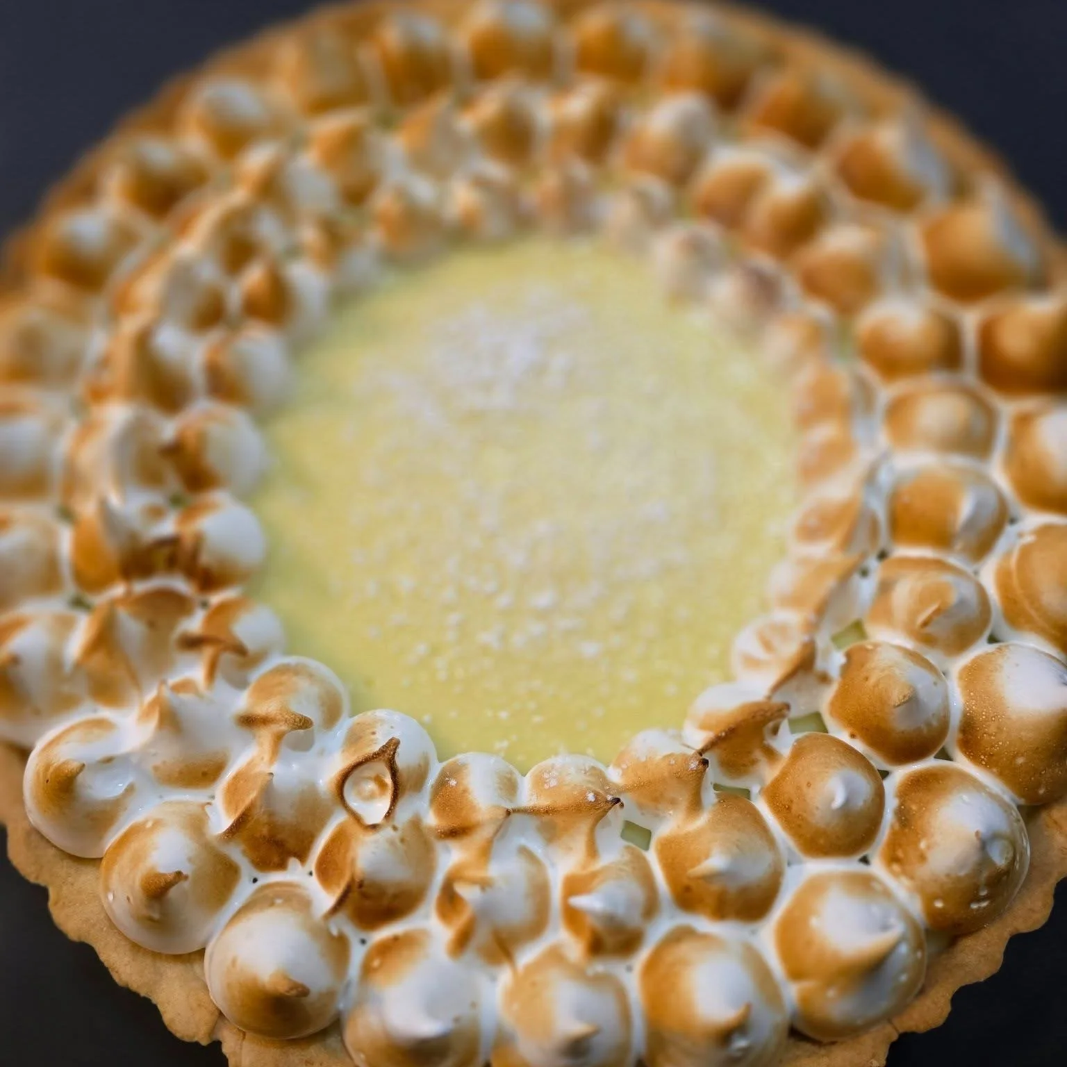 A close-up of a pie with a crust rim decorated with toasted meringue peaks surrounding a creamy filling.
