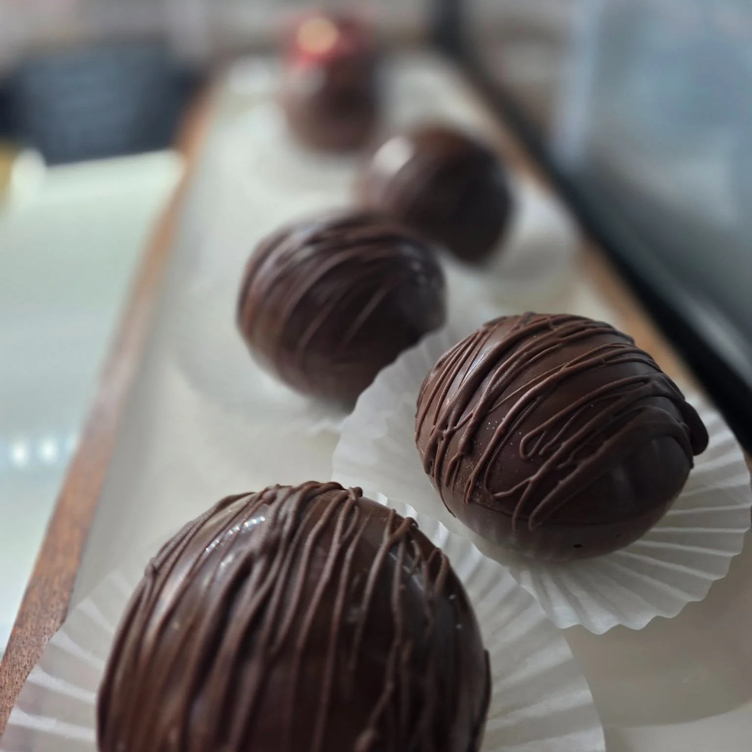 Chocolate truffles decorated with drizzles, displayed on a tray lined with white paper.