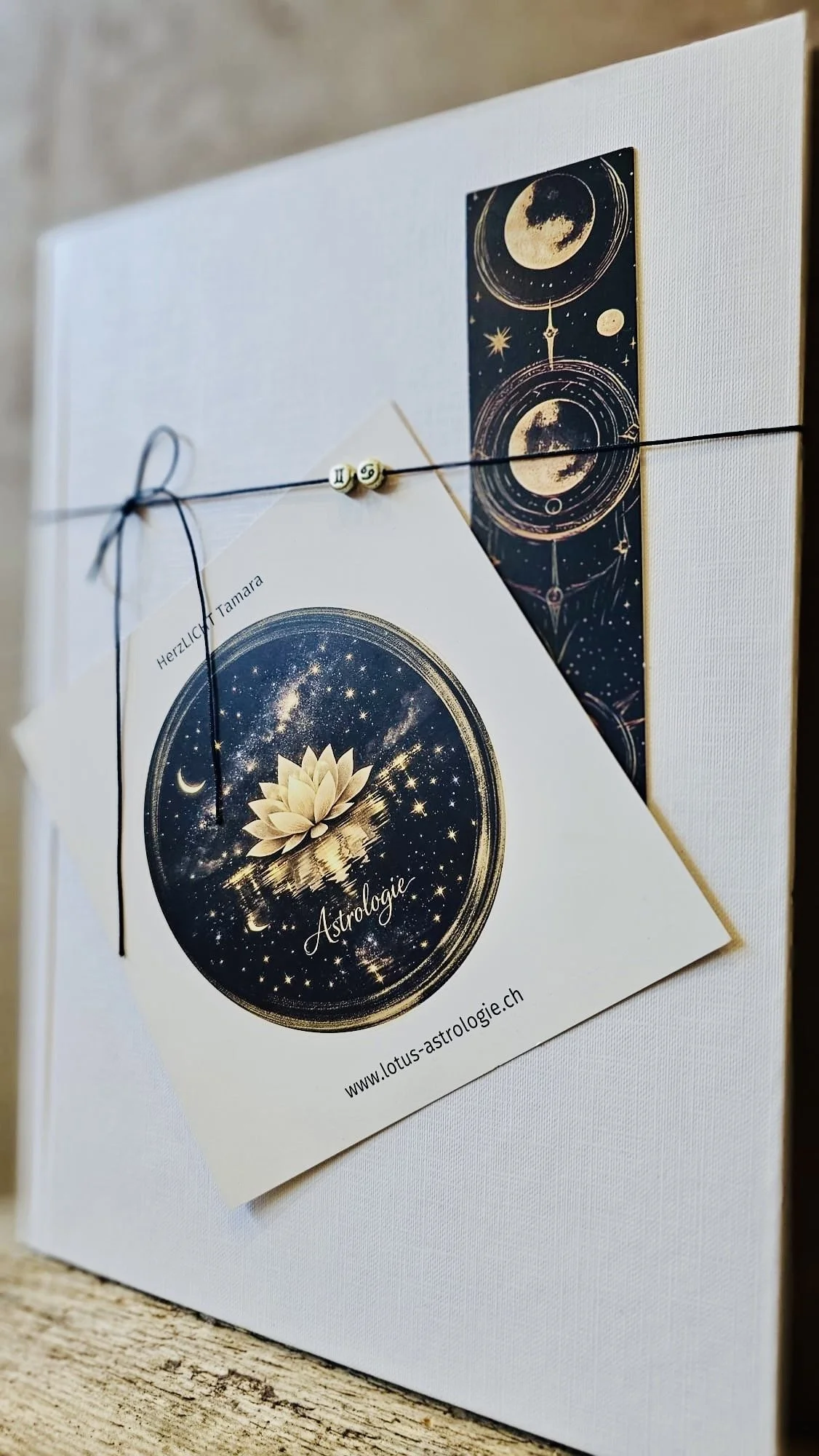 Weiße Leinwand mit Karte und Schlüsselband, das eine Karte mit Lotus-Symbol und Sternen, sowie ein Astrologie-Plakat mit Mond- und Sternmotiven zeigt.