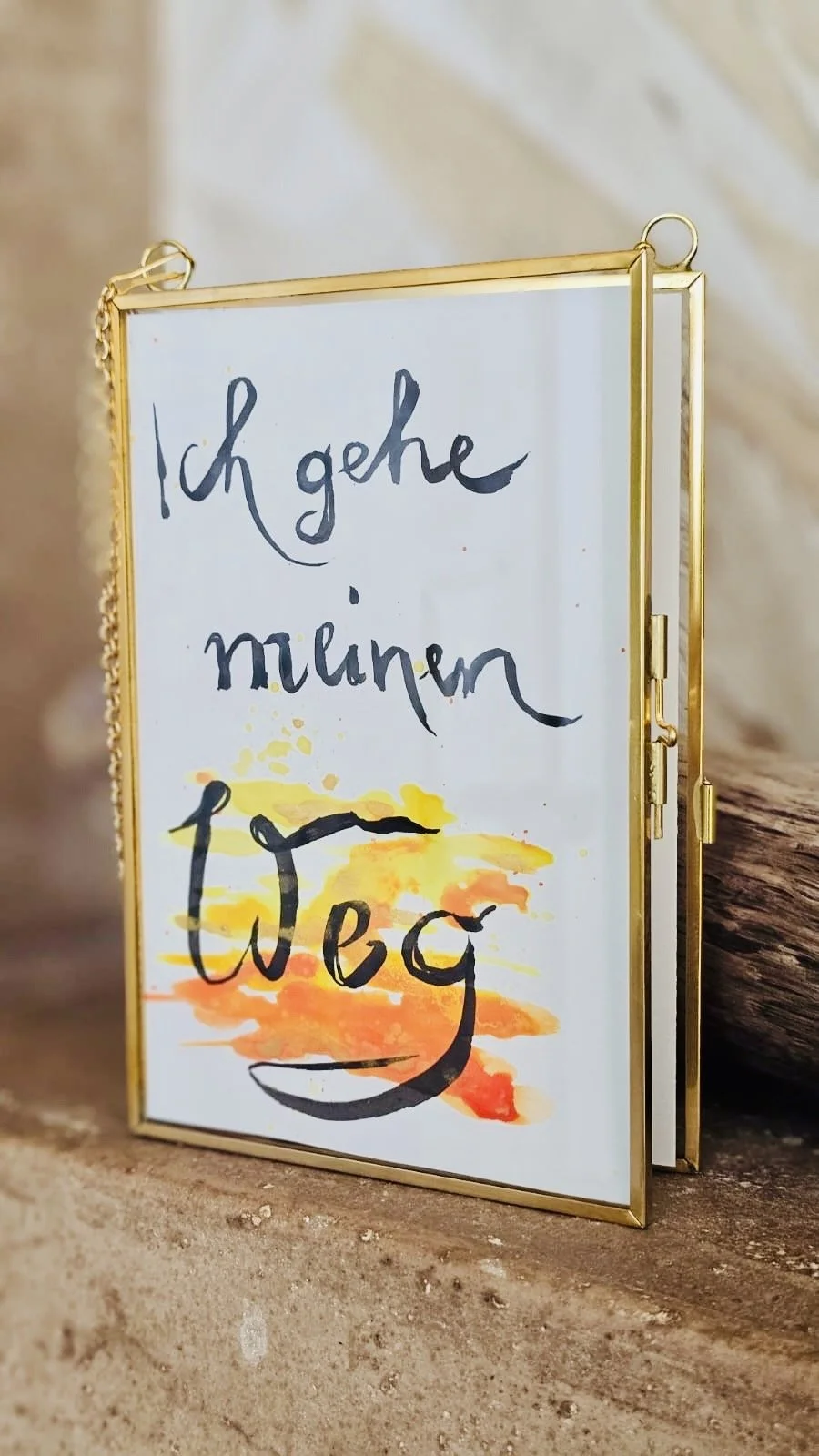 Ein handgeschriebener Zettel mit der Aufschrift 'Ich gehe in den Urlaub', vor einem goldfarbenen Rahmen, auf einem Holzuntergrund.