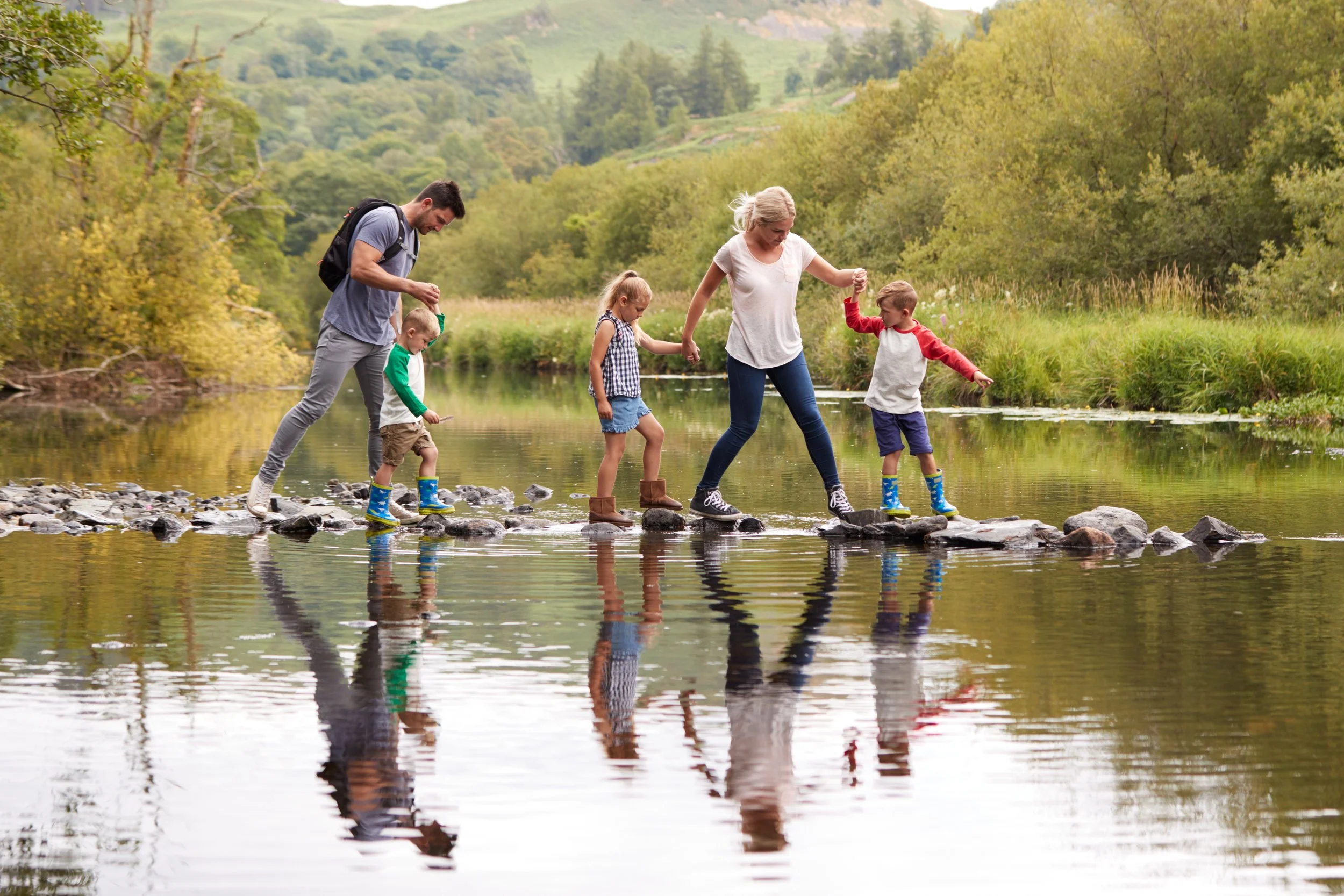A family with small children walking over stepping stones across a creek