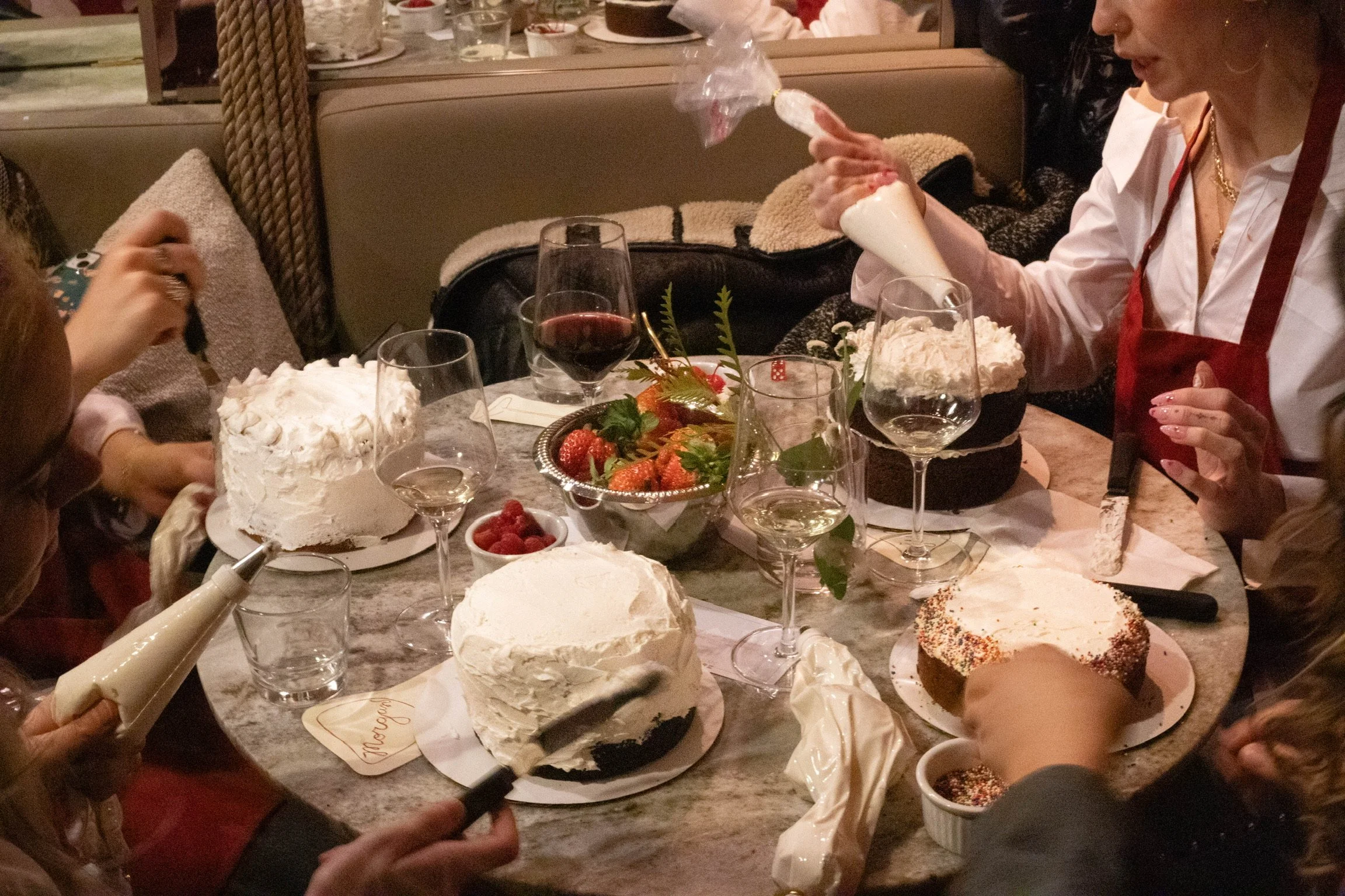 People gathered around a table celebrating with cakes, strawberries, raspberries, and glasses of wine.