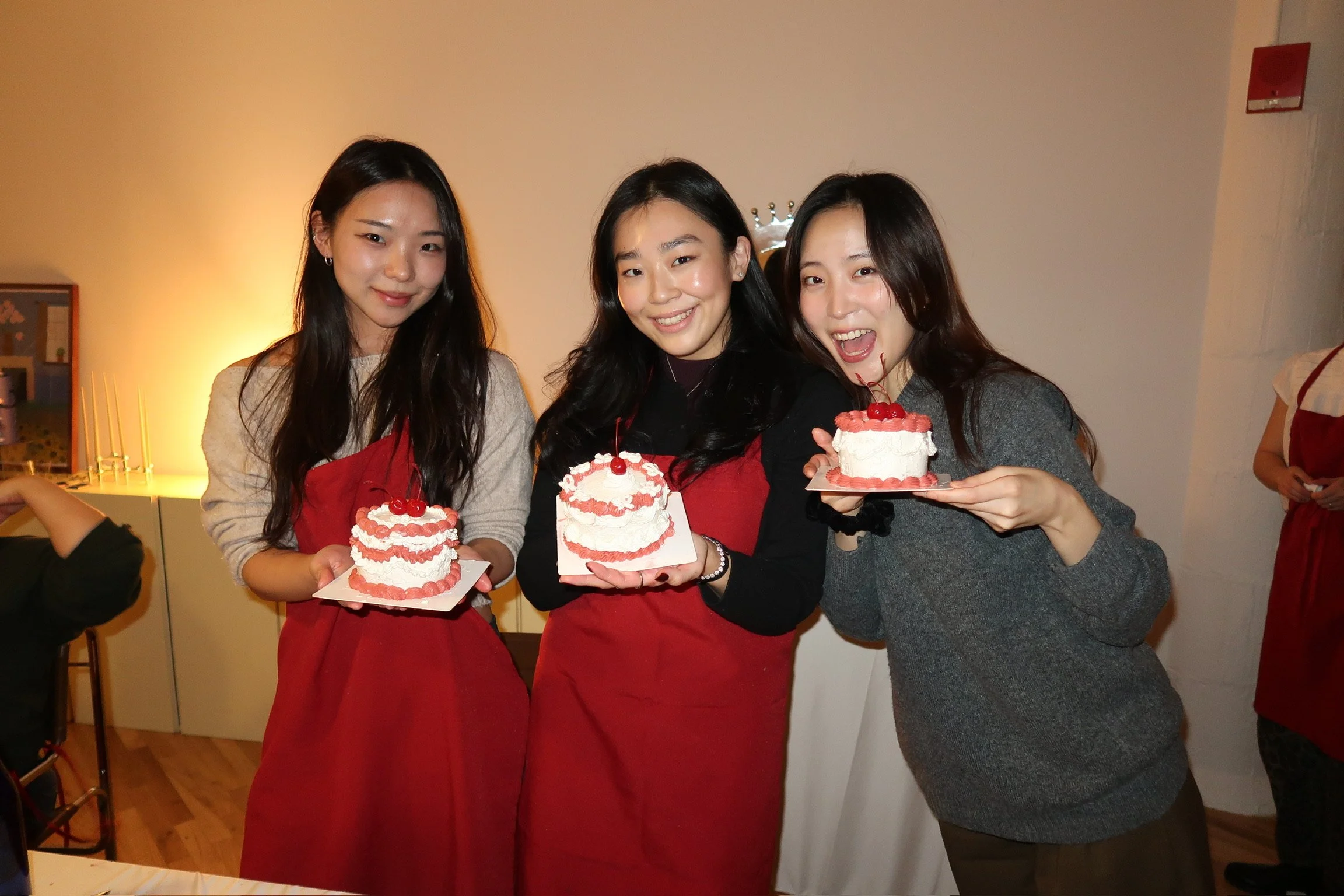 Three women holding small cakes with cherries, smiling at a celebration.