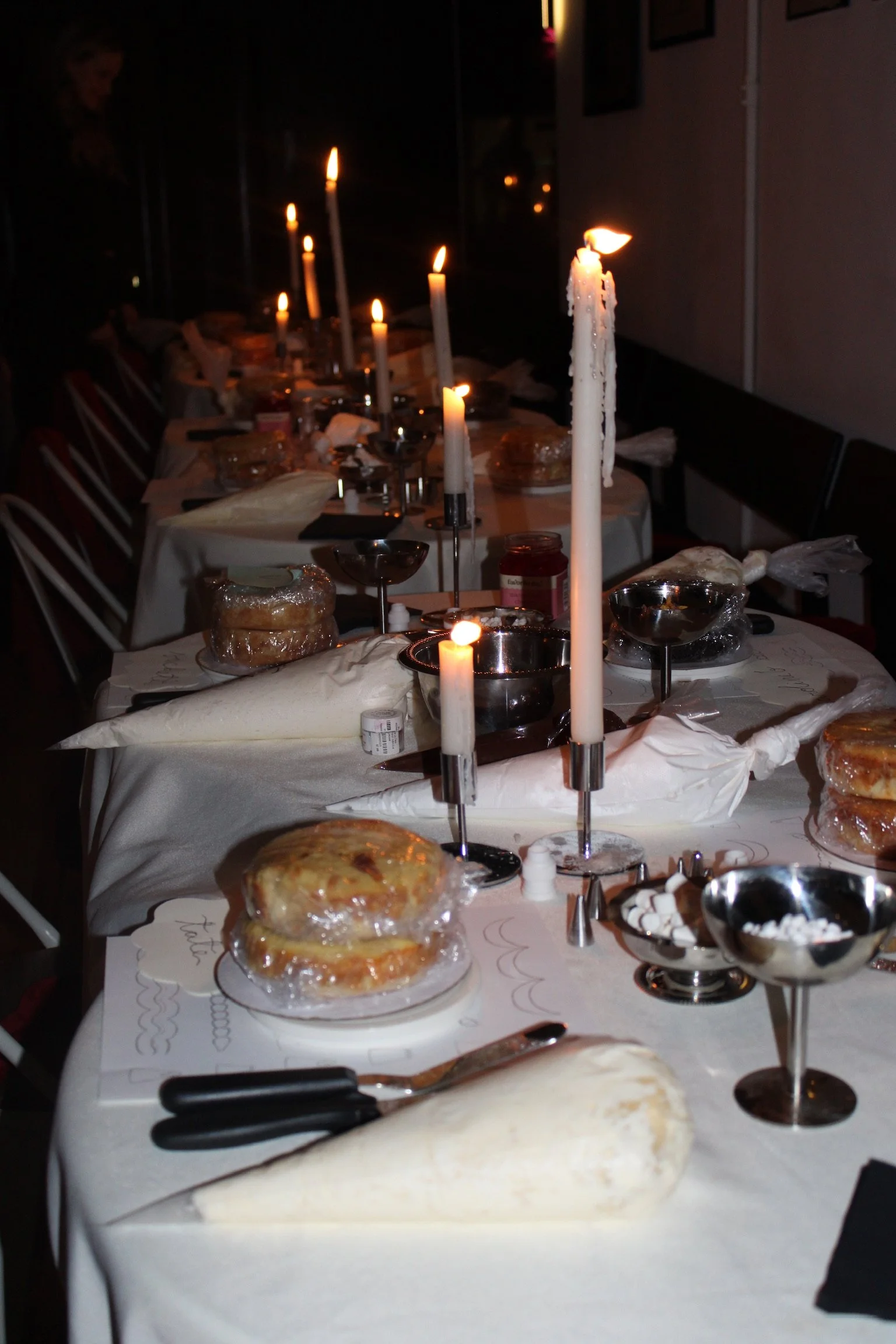 A dimly lit table set for a celebration with candles, cakes, and various dishes, likely for a birthday or special occasion.
