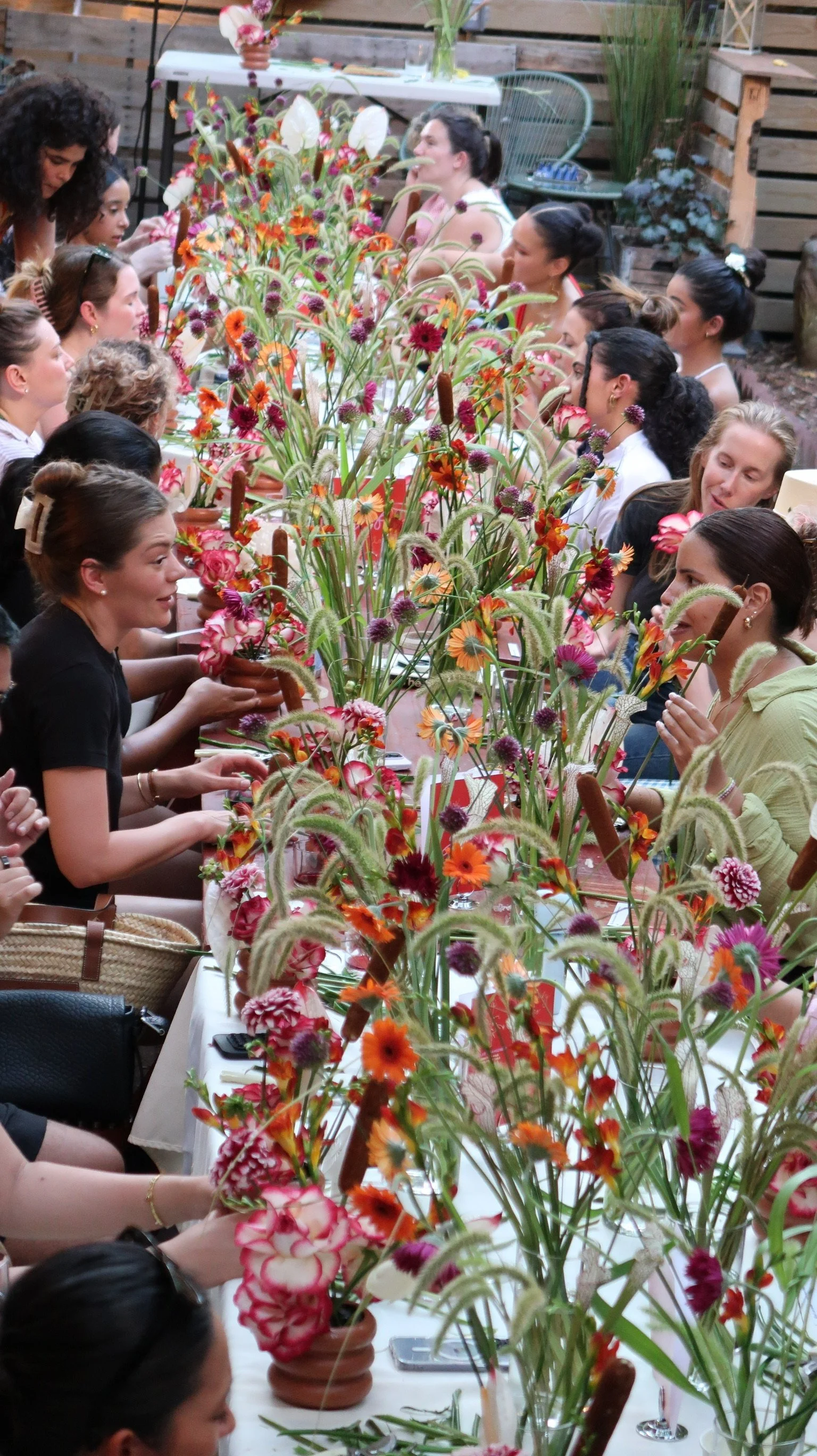 Group of women sitting at a long table decorated with a variety of vibrant flowers in small pots.