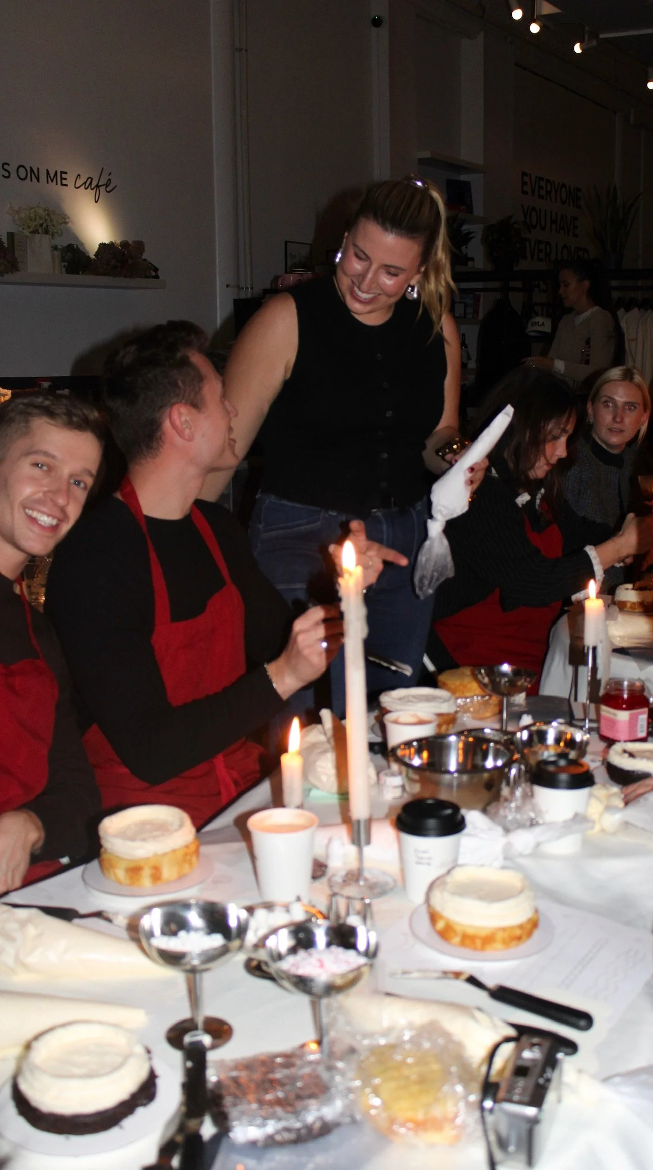 People celebrating birthday at a dining table with cakes, candles, and coffee cups in a cozy indoor setting.