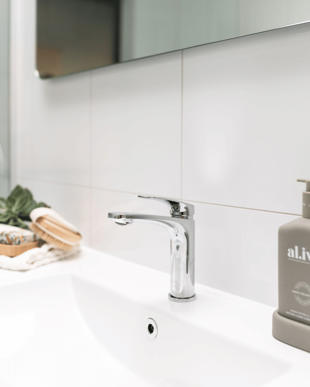 Bathroom sink with chrome faucet, soap dispenser, and toiletries on countertop.