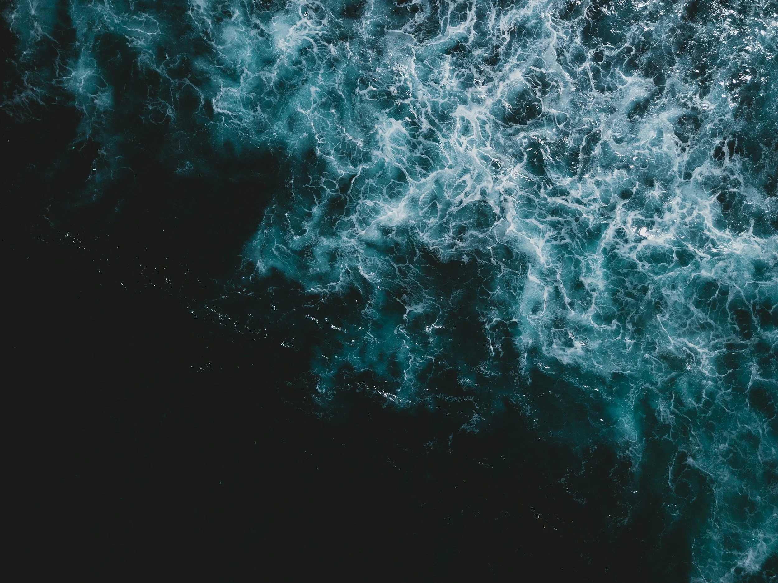 Aerial view of ocean water with blue waves and white foam.