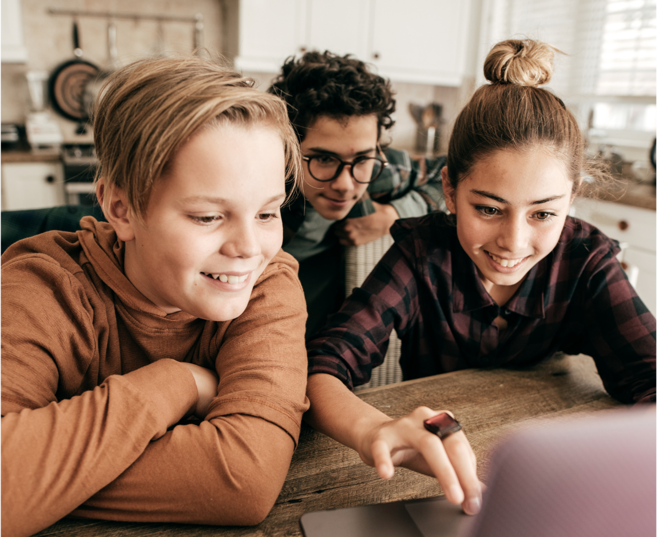 Three kids and an adult looking at a laptop screen together in a kitchen.
