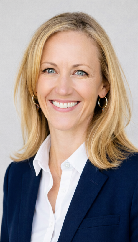A professional woman with blonde hair, wearing a navy blazer and white shirt, smiling against a light gray background.