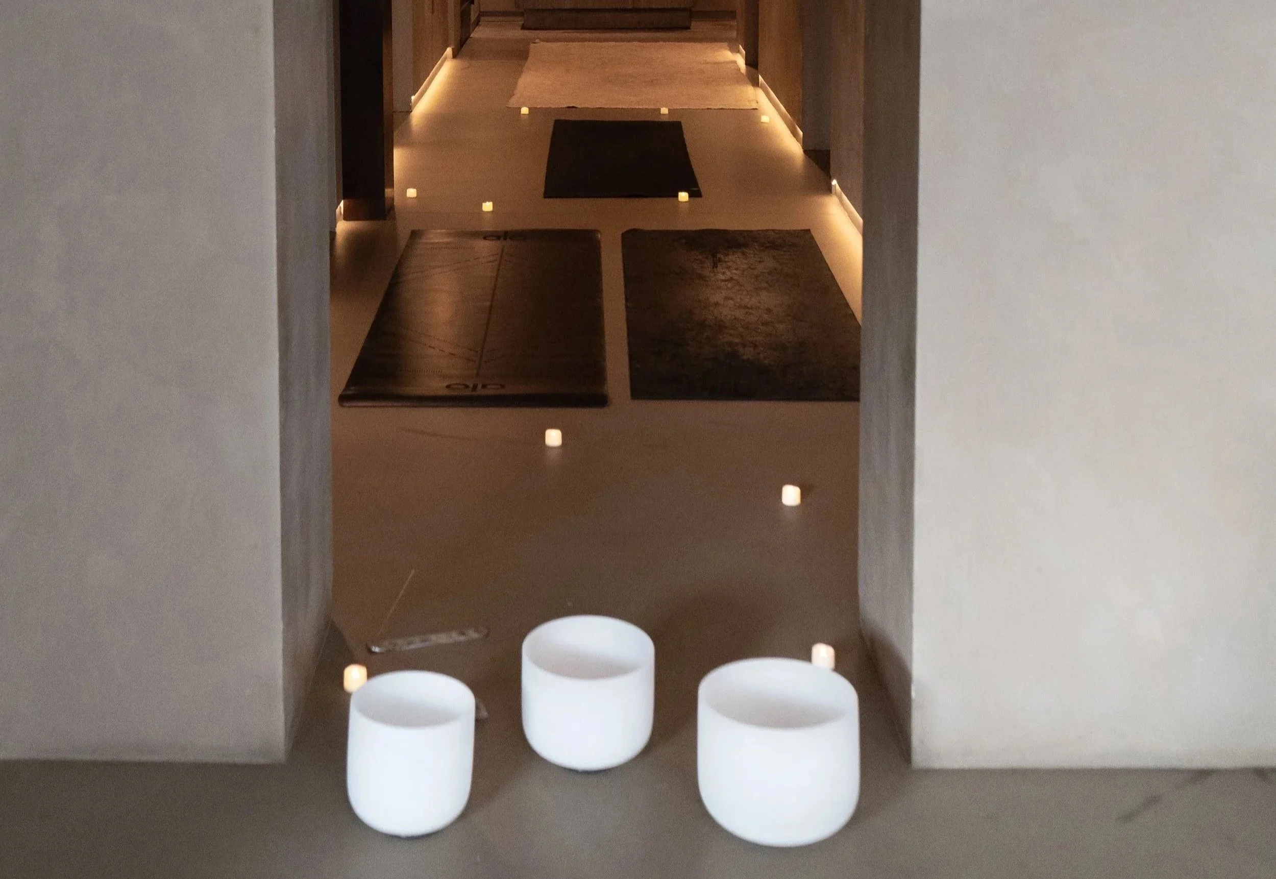 Interior view of a yoga or meditation studio with mats laid out on the floor, surrounded by small candles and illuminated by subtle lighting.
