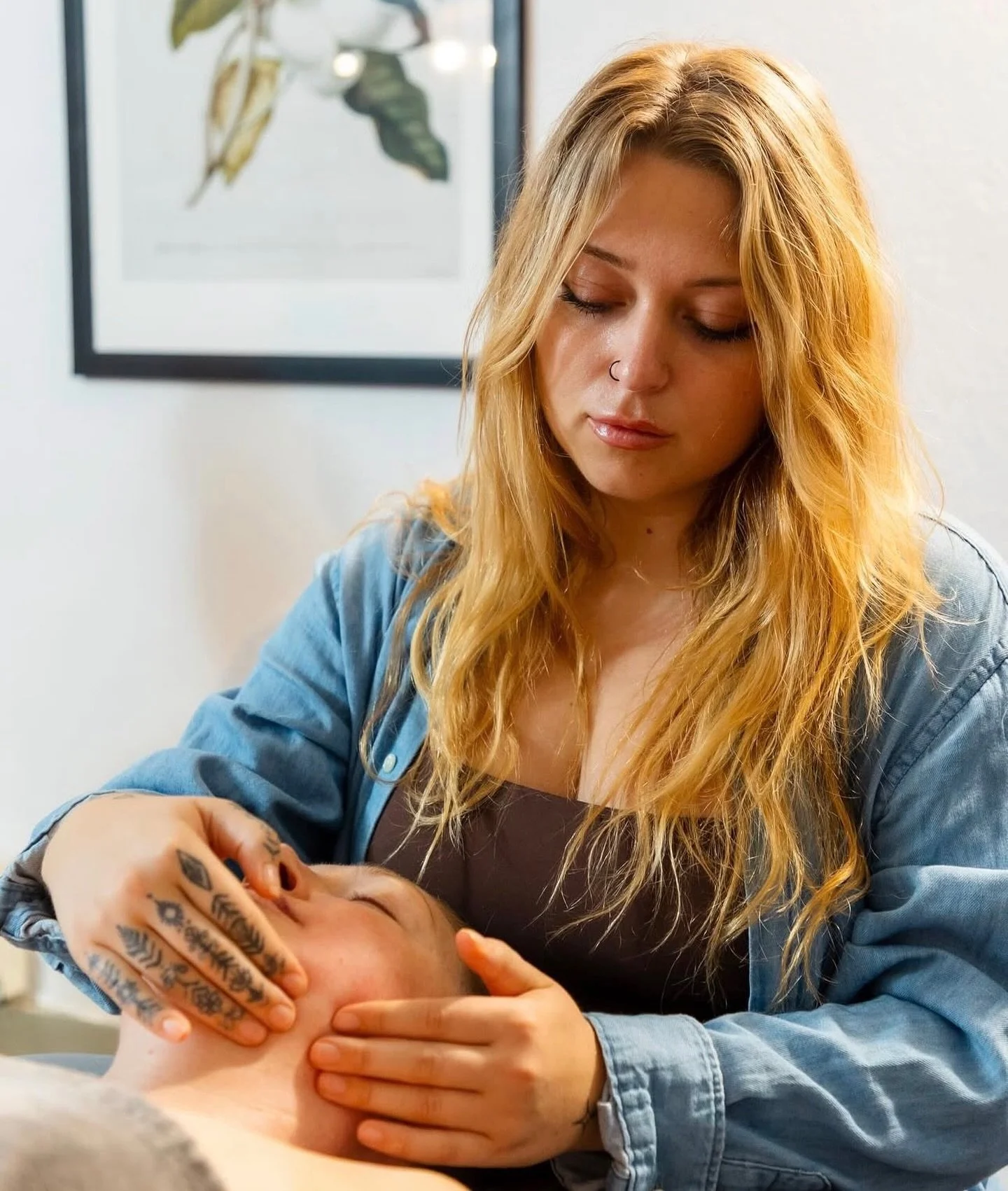 A woman giving a facial massage to a person lying down with eyes closed.
