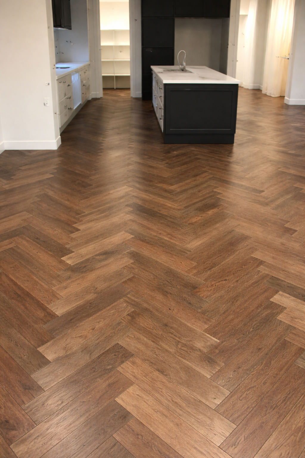 Empty kitchen with herringbone wood floor, white walls, black kitchen island, and open shelving in the background.