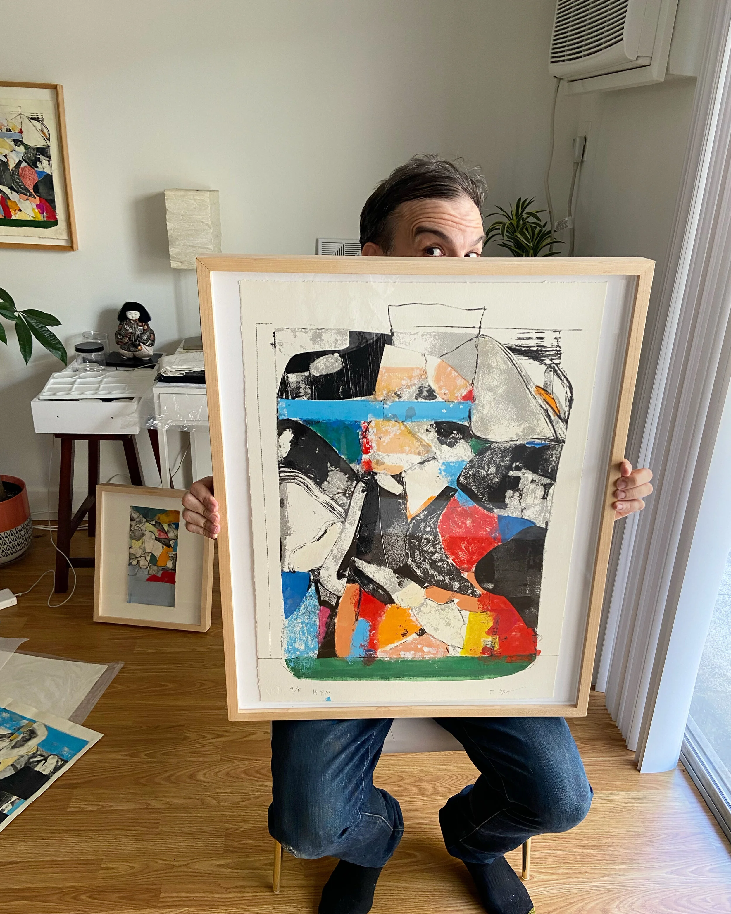 Person holding a colorful abstract artwork in a wooden frame, peeking over the top of it.