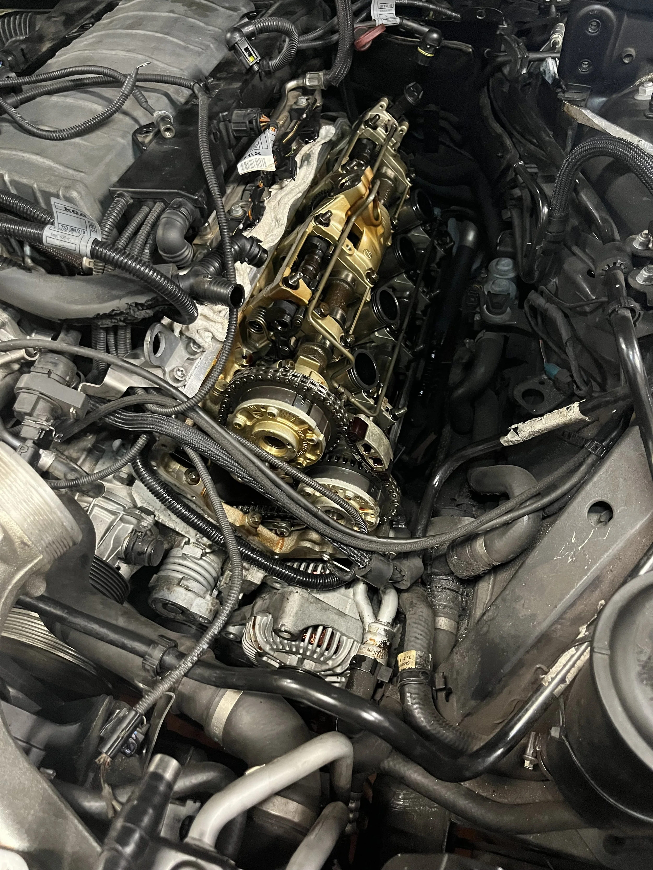 Close-up view of a car engine with various mechanical and electrical components, hoses, and belts visible.