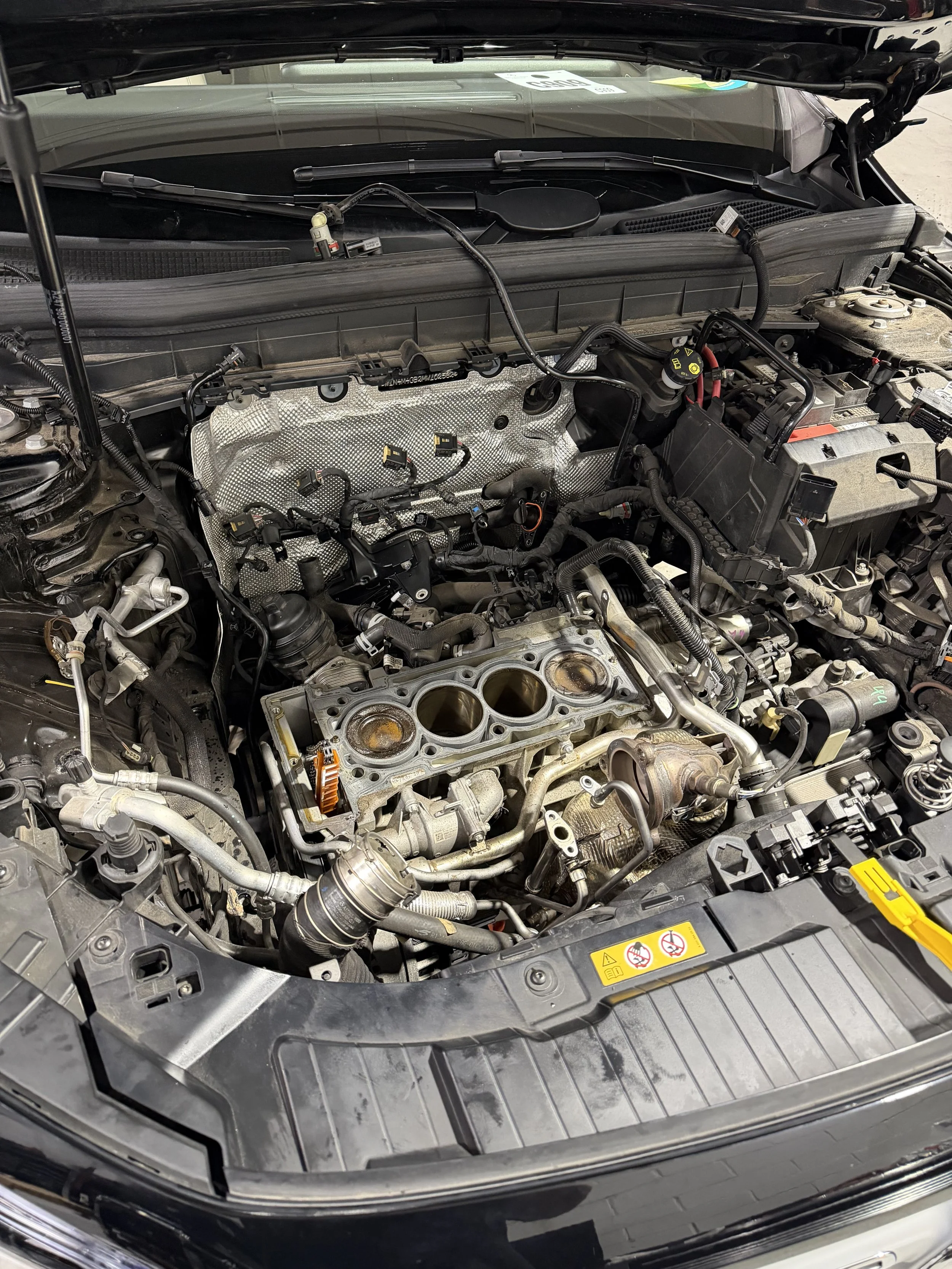 Close-up of a car engine bay, with the engine cover removed, showing various engine components, hoses, and wiring.