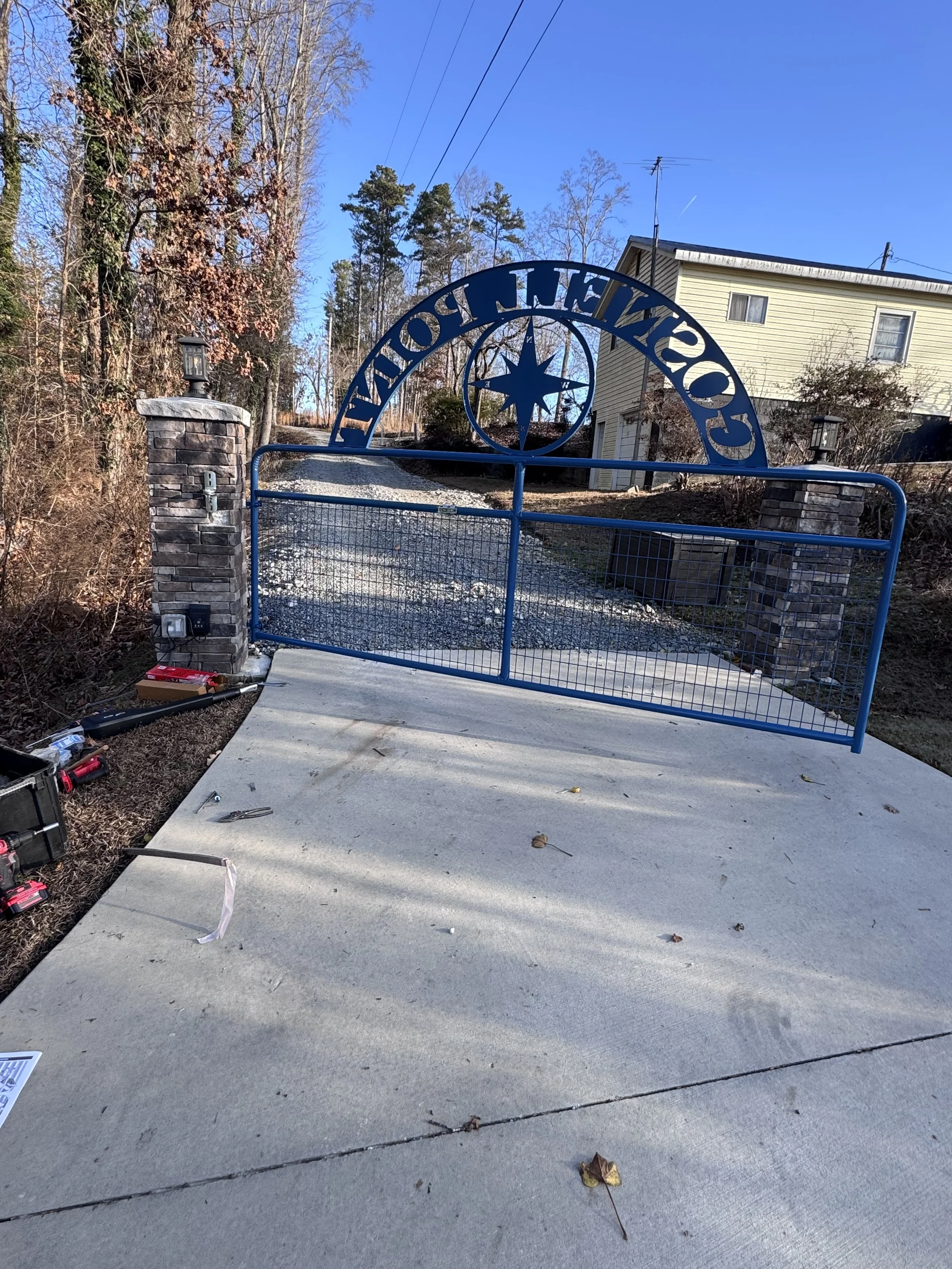 Blue metal gate with 'COWETA COUNTY' written at the top, flanked by stone pillars, at the entrance to a driveway