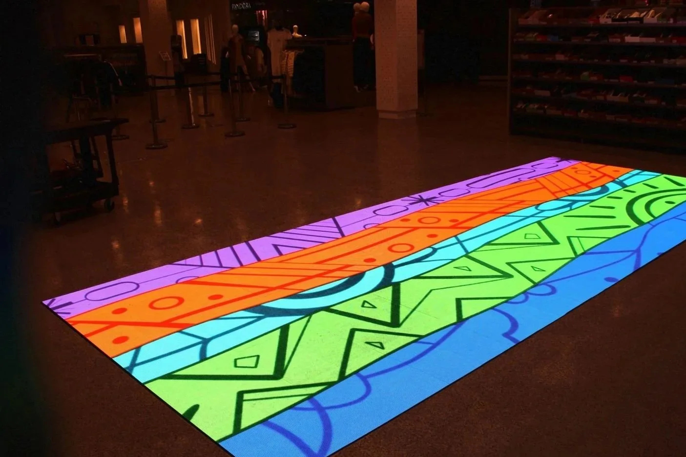 Colorful illuminated interactive floor display with geometric and abstract patterns in a dimly lit indoor space.