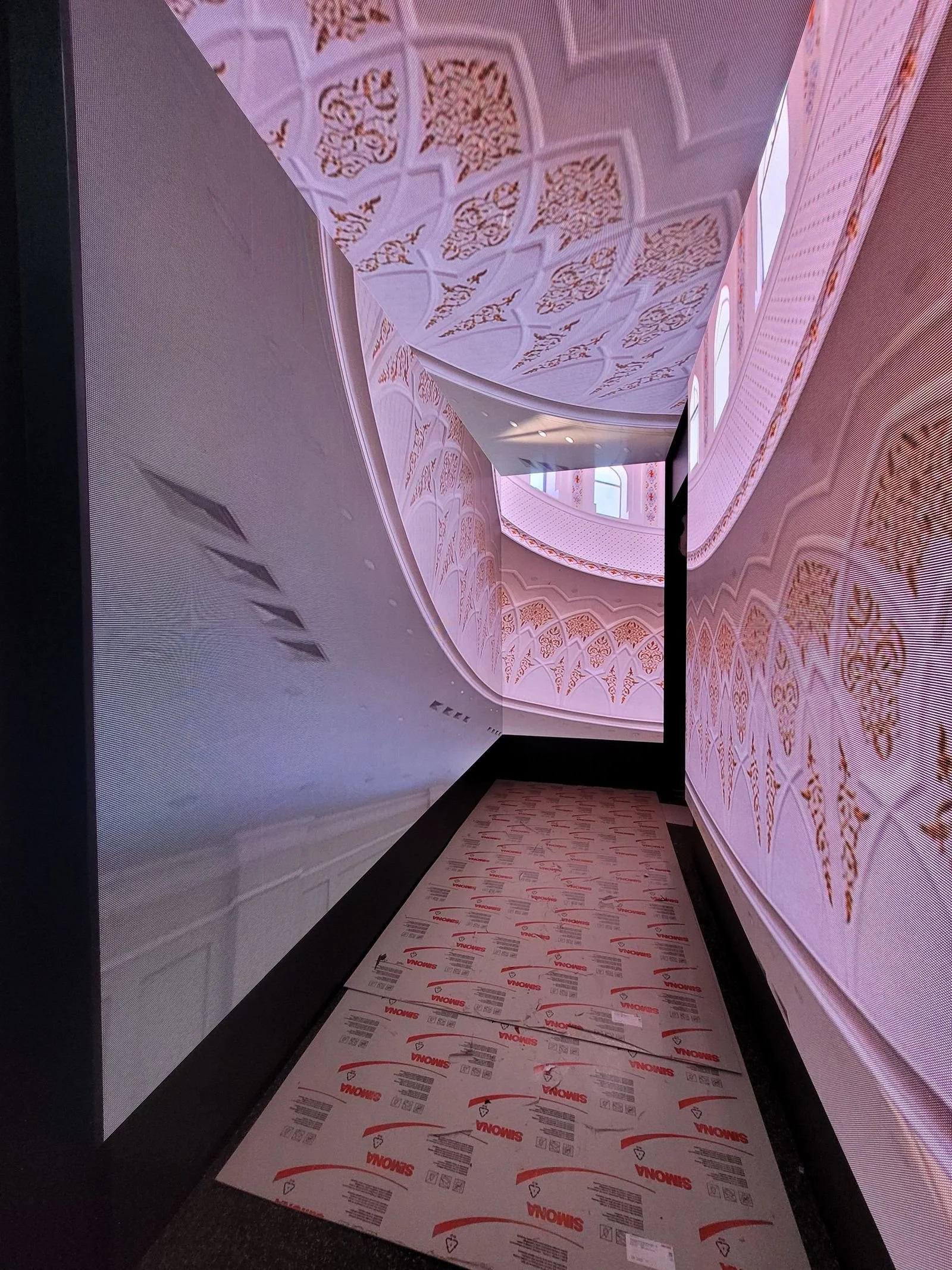 Interior of a building with curved, ornate pink and gold decor, large windows, and reflective surfaces.