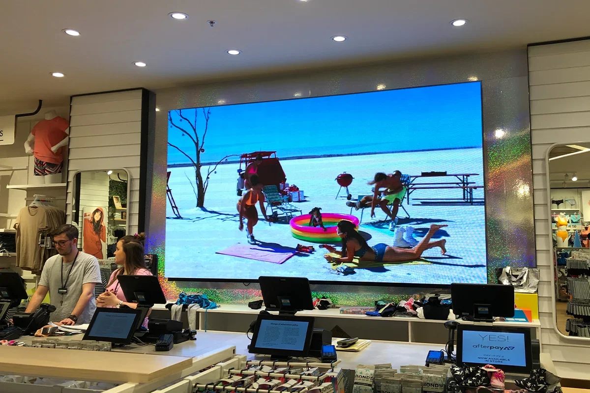 Large digital screen showing people at a beach on snow, with an inflatable pool, a dog, and beach chairs.
