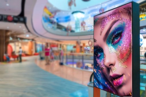 Large digital screen displaying a close-up of a woman's face with colorful, glittery makeup in a shopping mall.
