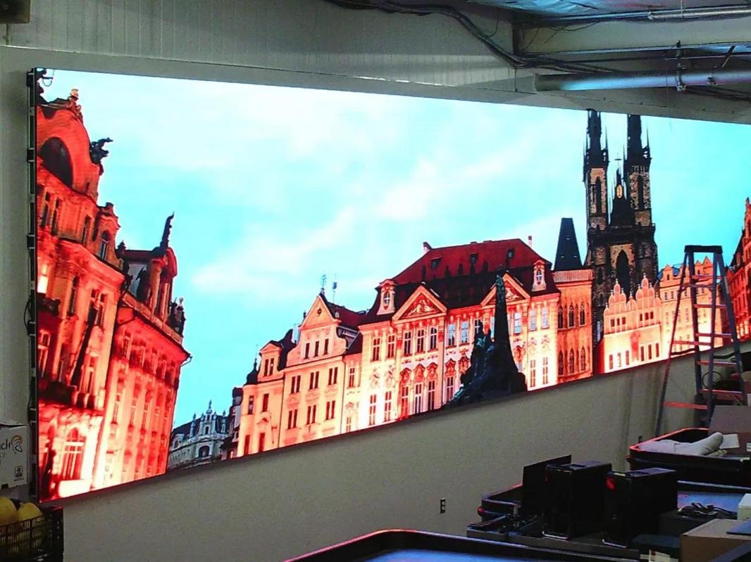 Large LED screen displaying an image of historic European buildings with a prominent church tower, under a partly cloudy sky.