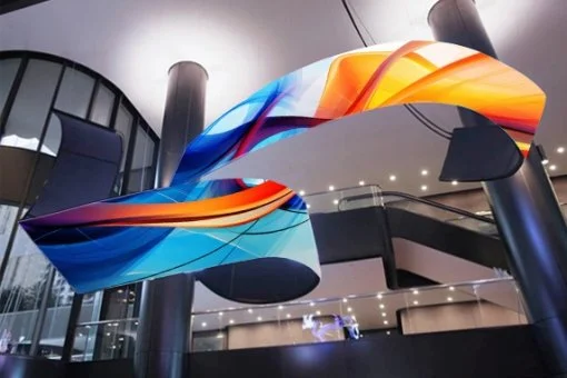 Modern indoor space with a colorful abstract sculpture hanging from the ceiling, featuring blue, orange, and yellow curved elements.